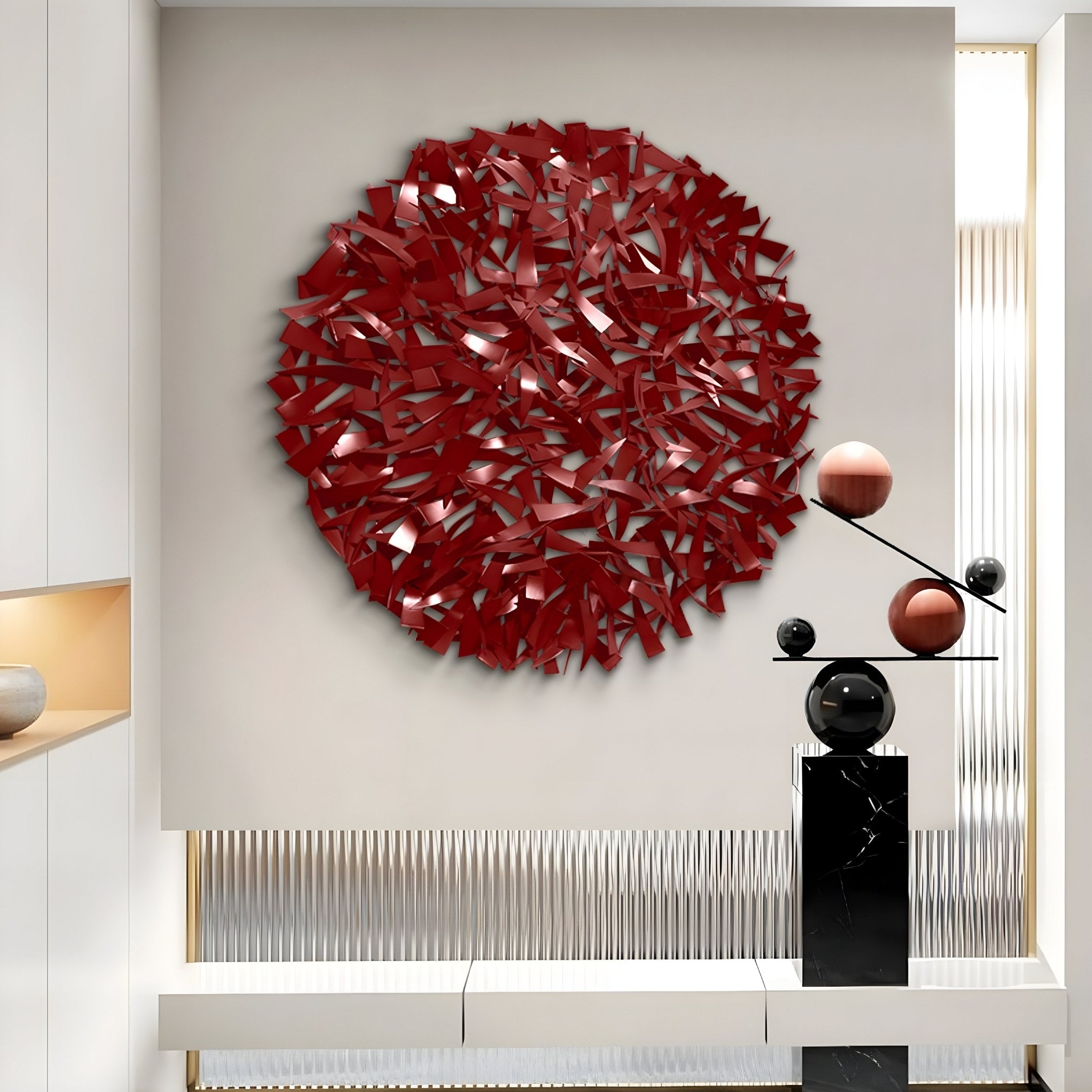 The Eclat Sphere Red Abstract Metal Wall Art by Giant Sculptures exemplifies modern elegance mounted on a white wall. In the foreground, a contemporary black and white sculpture with red and black spheres rests on a cylindrical pedestal, creating a minimalist interior setting.