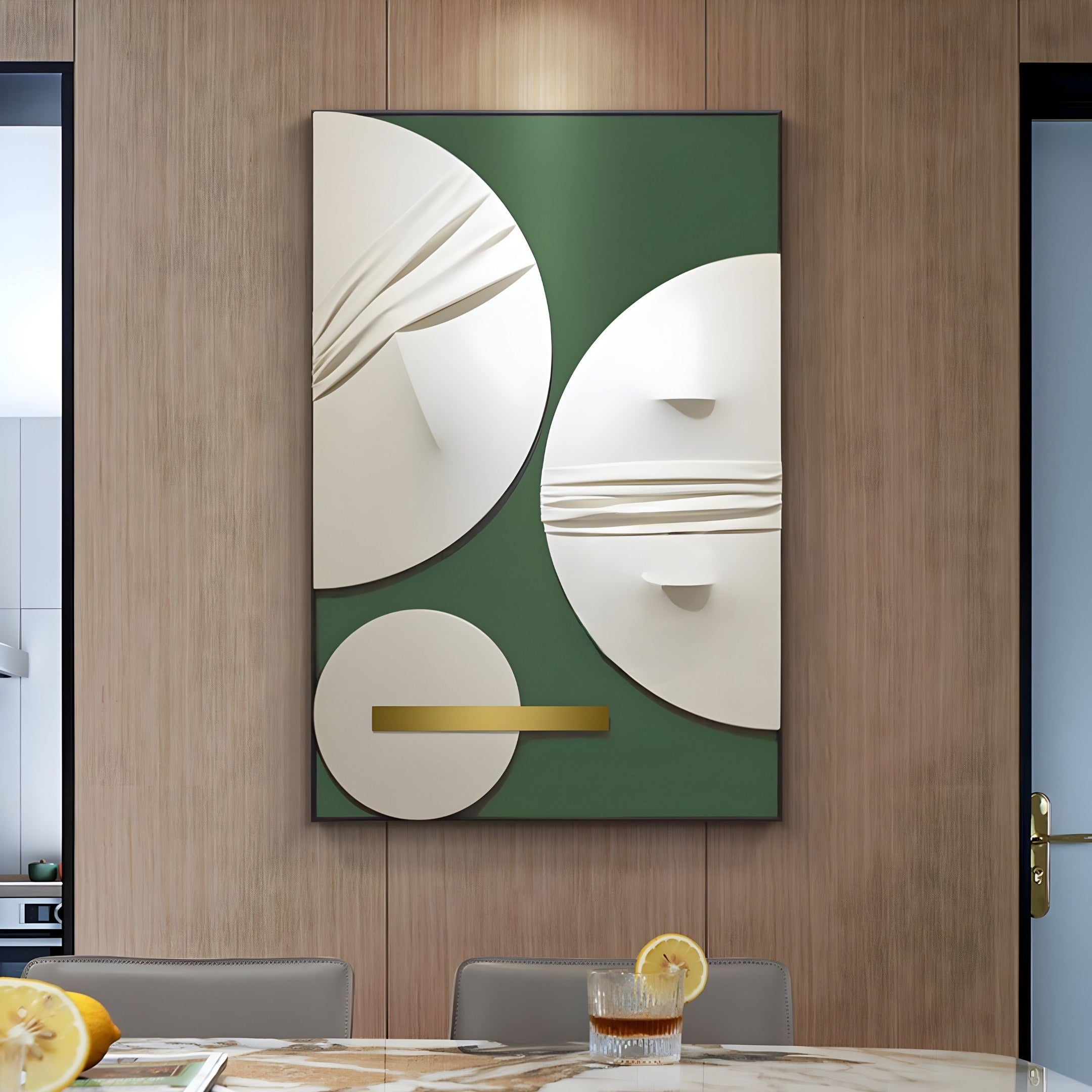 The Opus Green & Gold Accent Circular Geometric Leather 3D Wall Art by Giant Sculptures features large overlapping white circles and a horizontal gold bar on a dark green backdrop. A marble-topped table with a lemon water glass complements the green and gold accents.