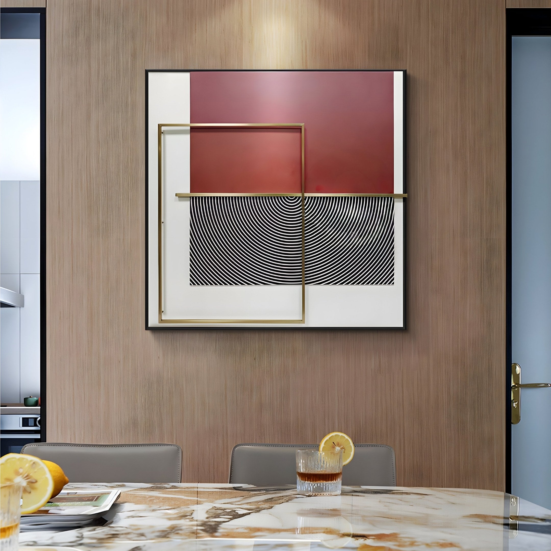 A modern dining room includes a marble table, two chairs, lemon-garnished drinks, and the Optique Spiral Black & Red Square Wall Art by Giant Sculptures framed in gold. A light wood and glass door enhances the contemporary vibe.