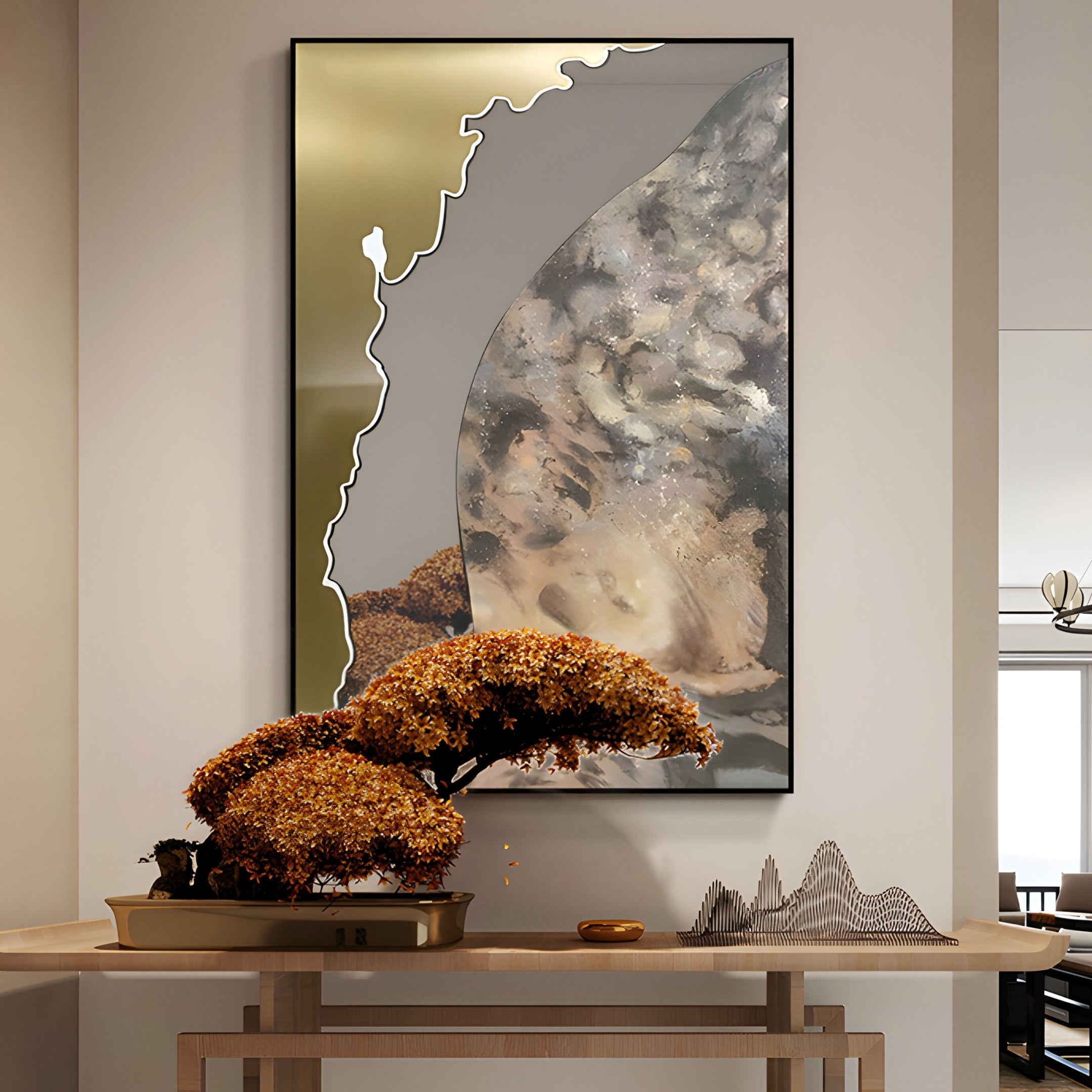 The Astrid Gold Edge Earthy Abstract Wall Art by Giant Sculptures hangs above a small table holding an autumn-leaf bonsai and a peak-shaped sculpture, imparting a sleek, minimalist aesthetic to the modern living space.