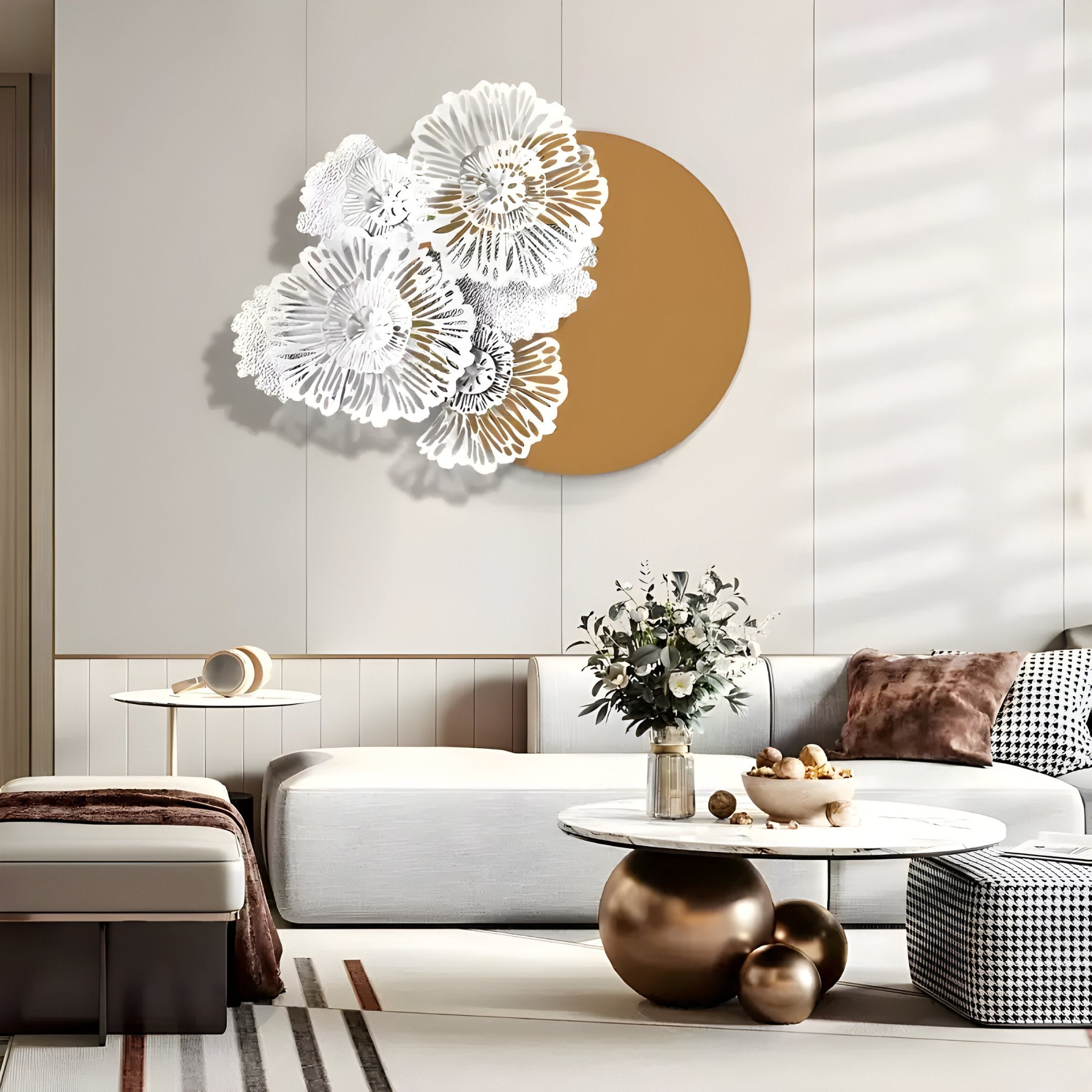 A modern living room showcases a white couch, patterned pillows, and a circular marble coffee table. The wall is adorned with the striking Fleur Halo Mustard Round White Metal Floral Decorative Wall Art by Giant Sculptures. Sunlight streams in, enhancing the serene ambiance with soft shadows.