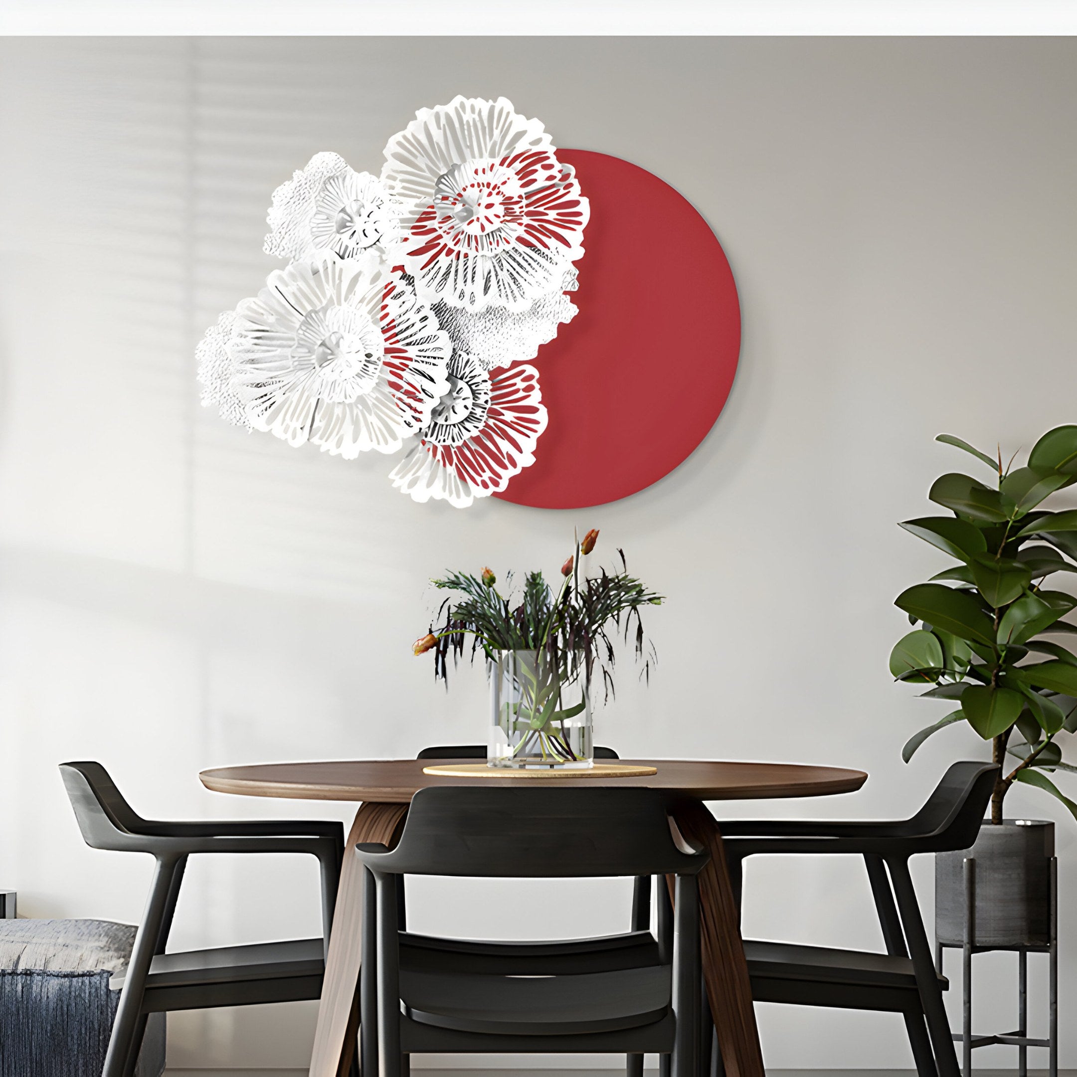 A modern dining room features a round table with four chairs and a flower vase. On the wall, the Fleur Halo Red Round White Metal Floral Decorative Wall Art by Giant Sculptures showcases white metal flowers with a red circle. A tall green plant enhances the serene ambiance.