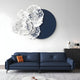 A modern living room features a dark blue sofa with an orange pillow, adorned by the Fleur Halo Navy Blue Round White Metal Floral Decorative Wall Art from Giant Sculptures. A black sideboard supports a lamp and sculpture, enhancing the minimalist contemporary decor.