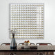 A dining table features a striped blue vase with dried plants and a bowl of apples. Behind it hangs the Giant Sculptures Lyselle 3D Ceramic Wall Art, adorned with hand-applied gold foil accents, on a white wall. The table is surrounded by brown chairs.