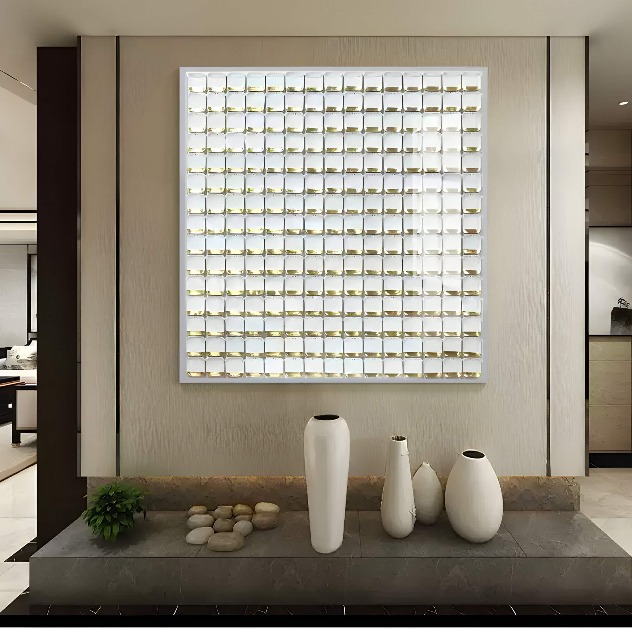 A modern interior features the Lyselle 3D Ceramic Wall Art by Giant Sculptures, showcasing its grid-like white tiles with hand-applied gold foil accents. Three tall white vases of varying sizes and a small plant rest on a dark marble shelf adorned with decorative stones.