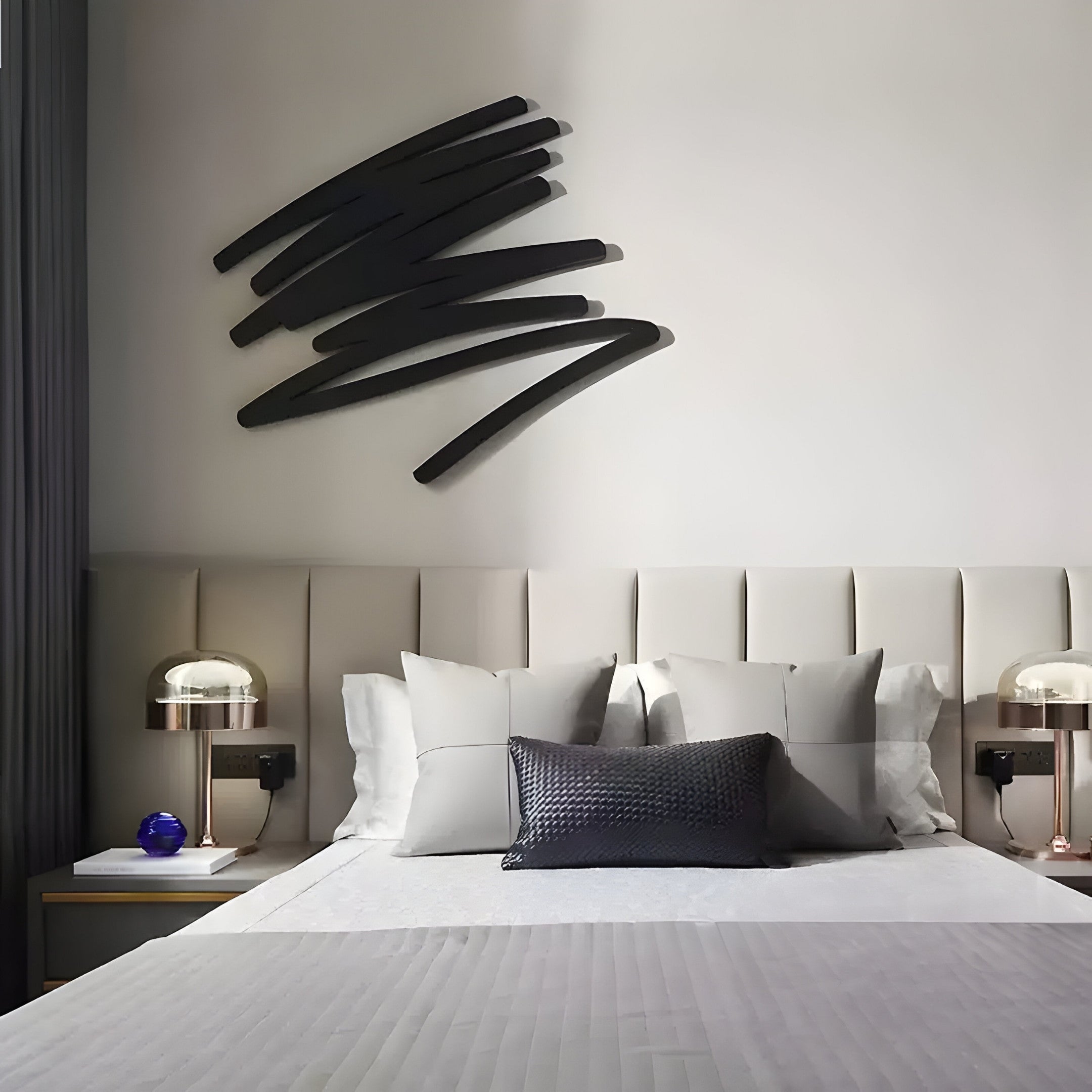 A minimalist bedroom features a modern bed adorned with white and gray bedding. Side tables hold two glass lamps, while the Giant Sculptures Oscura Stratum Layered Black Abstract Metal Wall Art adds abstract flair above the bed, enhancing the contemporary vibe of this neutral-toned space.