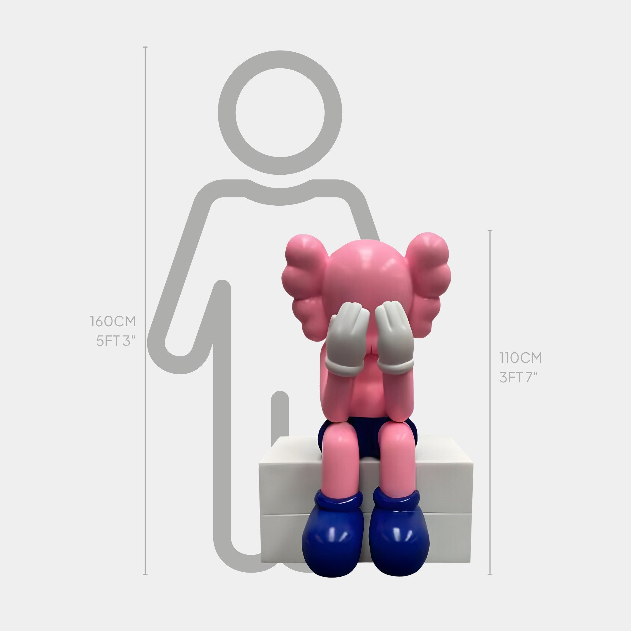 The Pedal Pink Iconify Melancholy Sitting Sculpture by Giant Sculptures shows a pink cartoon figure, hiding its face with white-gloved hands, seated on a white block. It features blue shoes, pink ears, and stands 110 cm tall against a gray human design—ideal for art-inspired spaces.