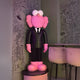 A large pink sculpture, the 130cm Black Suit Iconify CEO by Giant Sculptures, with big ears stands on a round pedestal. The rooms walls, covered in whimsical black-and-white doodles, add a modern artistic edge. Nearby, a high table with stools completes the luxury gallery vibe.