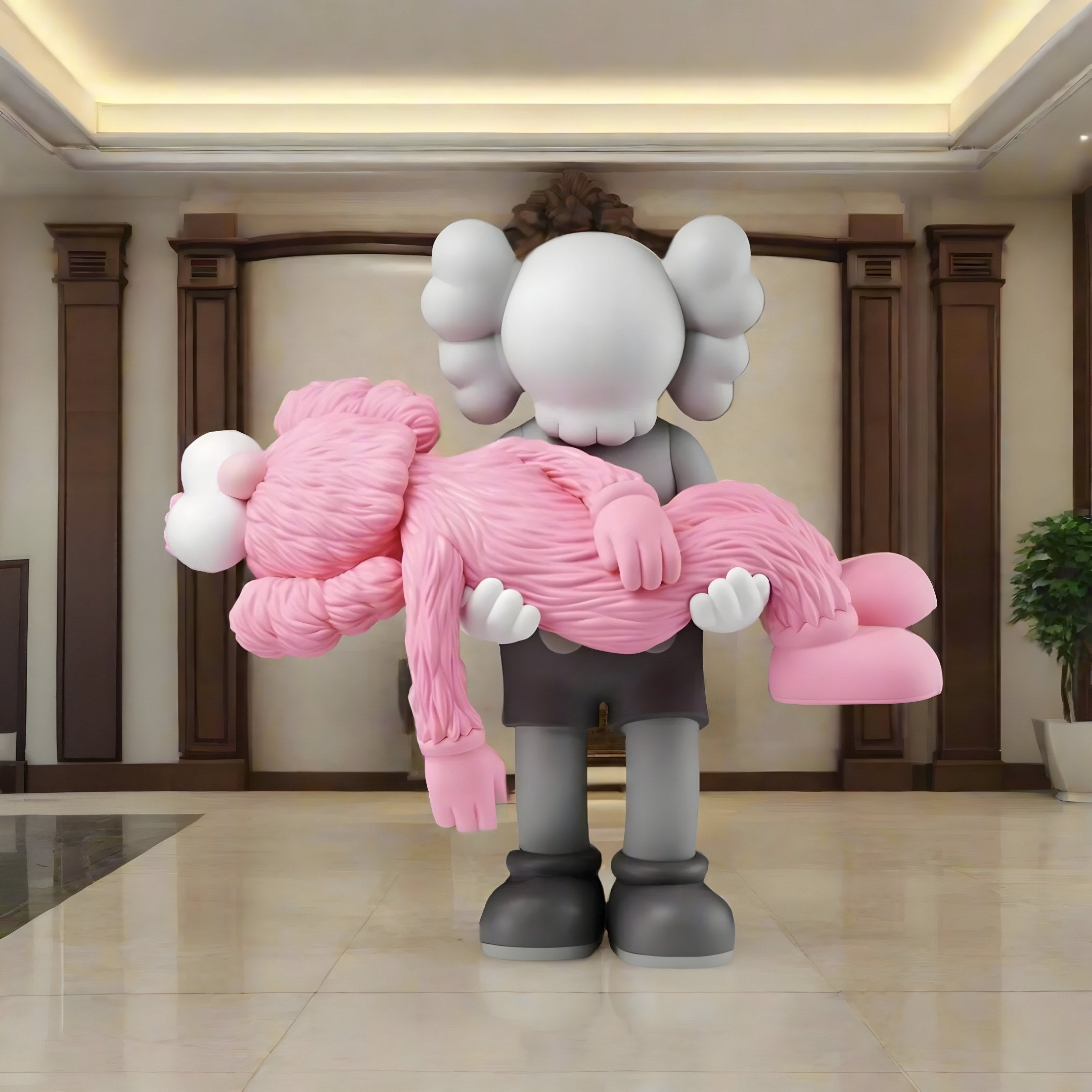 The Petal Pink Iconify Rescuing Furry Sculpture by Giant Sculptures (135cm) depicts a white-faced, gray-clad character tenderly holding another in pink. Showcased in an elegant indoor setting with high ceilings, columns, and a potted plant, it beautifully captures emotional connection.