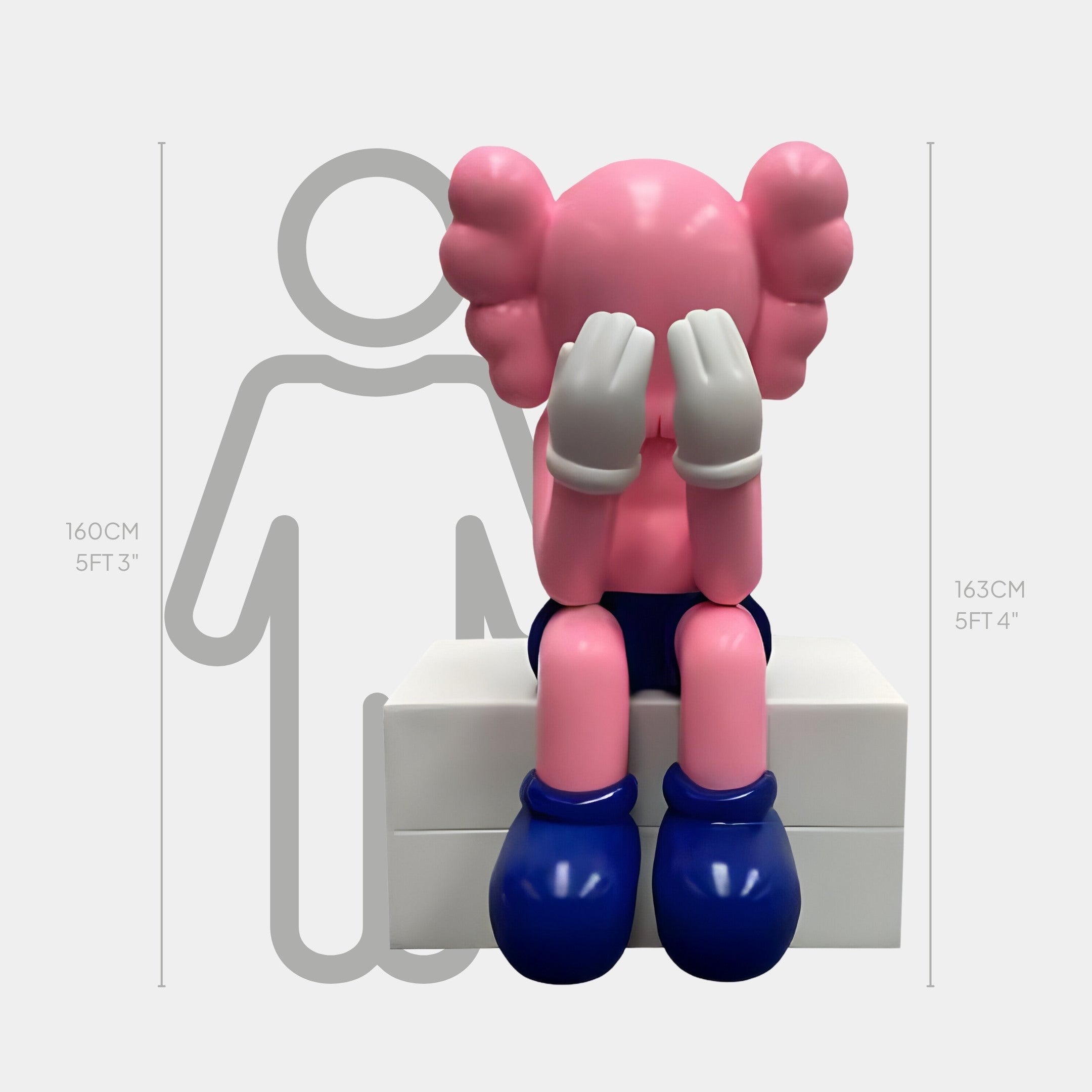 The Pedal Pink Iconify Melancholy Sitting Sculpture by Giant Sculptures depicts a character seated on a white block with large ears and gloves, covering its face as part of a modern art collection. Its height of 163 cm subtly interacts with an adjacently positioned silhouette.