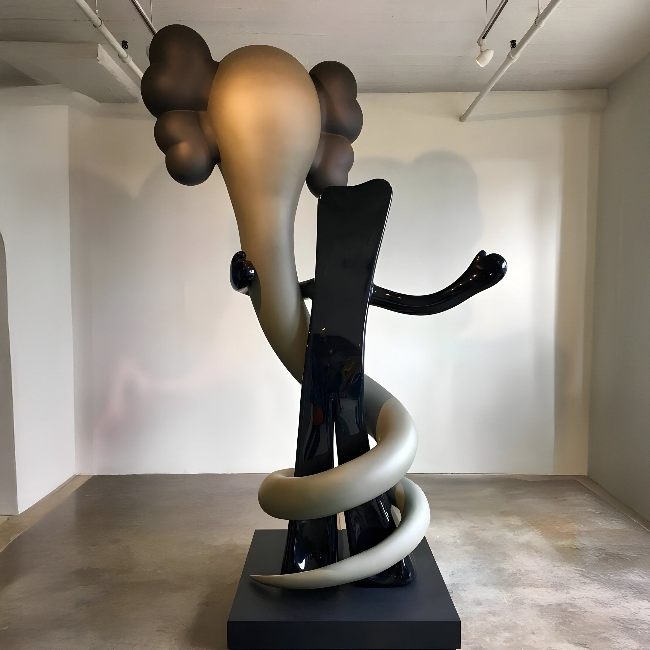 The Ash Grey Iconify Snake Sculpture by Giant Sculptures, standing at 176cm, features two abstract figures with exaggerated limbs and cloud-like heads in a minimalist gallery. One is glossy black; the other is crafted from resin in a gray gradient.