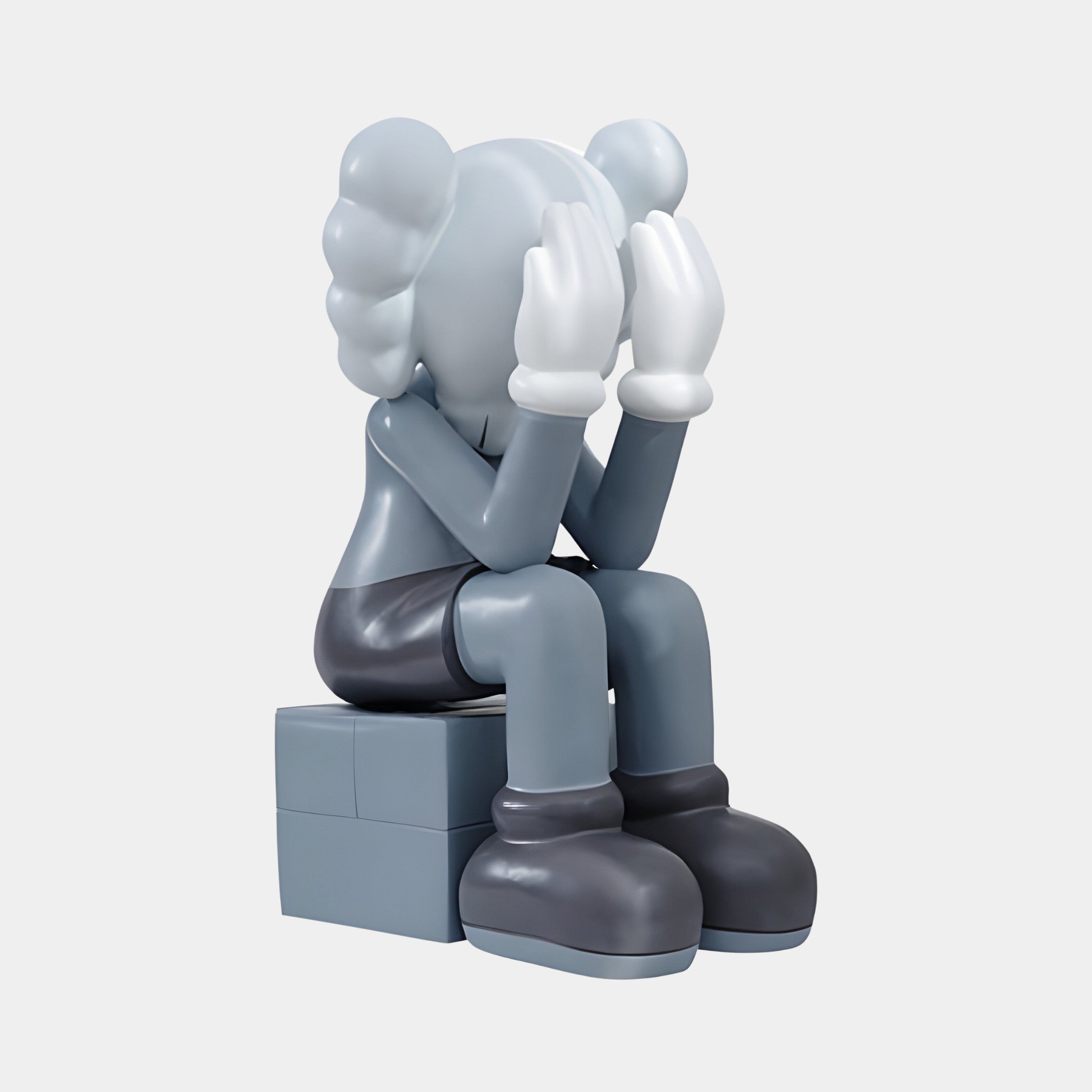 The Slate Grey Iconify Melancholy Sitting Sculpture by Giant Sculptures features a stylized character with large hands and an expressive pose. Its grey body, head buried in hands, symbolizes sadness or frustration against a white background, embodying modern minimalism at 70cm tall.