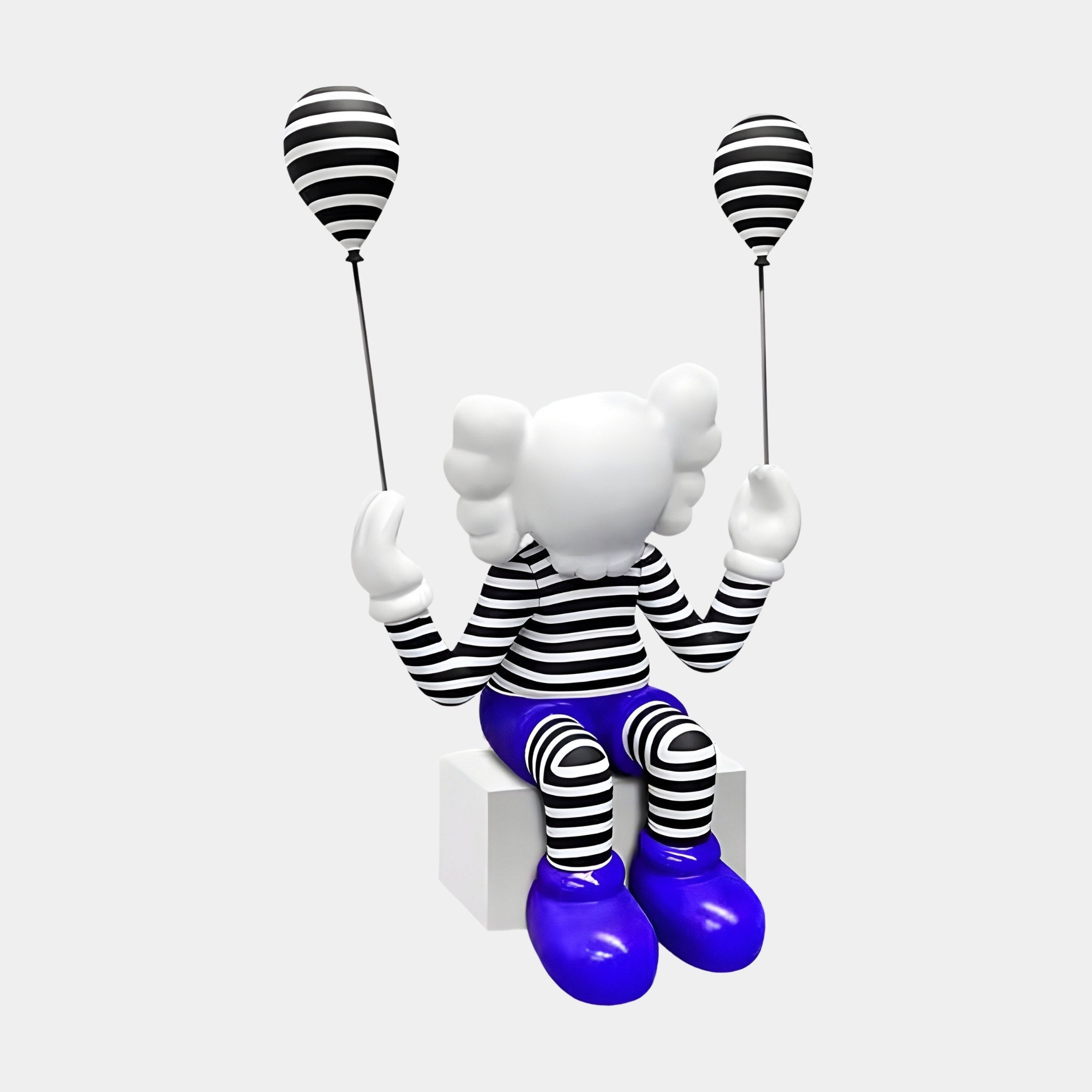 The Deep Blue Iconify Mime Sitting Sculpture by Giant Sculptures features a figure with a white head, black and white striped outfit, and blue shoes seated on a white cube. It holds two striped balloons, creating a striking contrast against the plain backdrop—perfect for contemporary interiors.