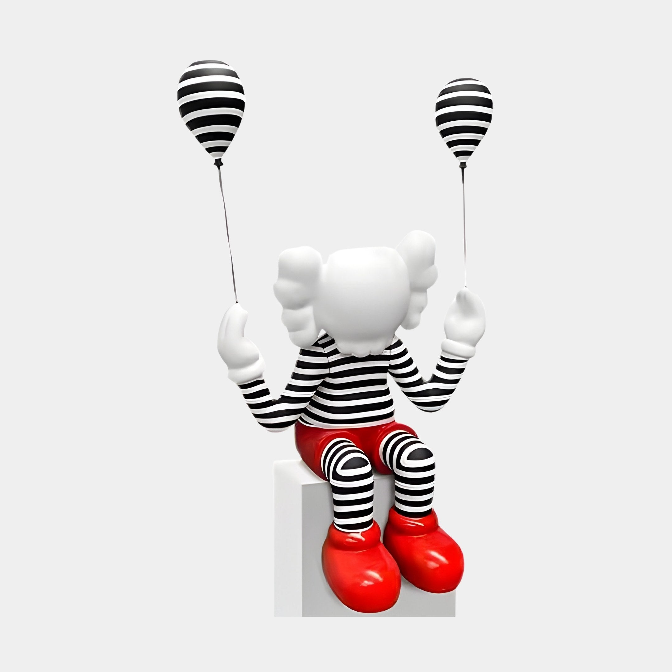 The Lustrous Red Iconify Mime Sitting Sculpture by Giant Sculptures features a smooth white head without facial features, dressed in black-and-white stripes with red shoes. Seated on a white block holding two striped balloons, this 70cm piece exudes charm.