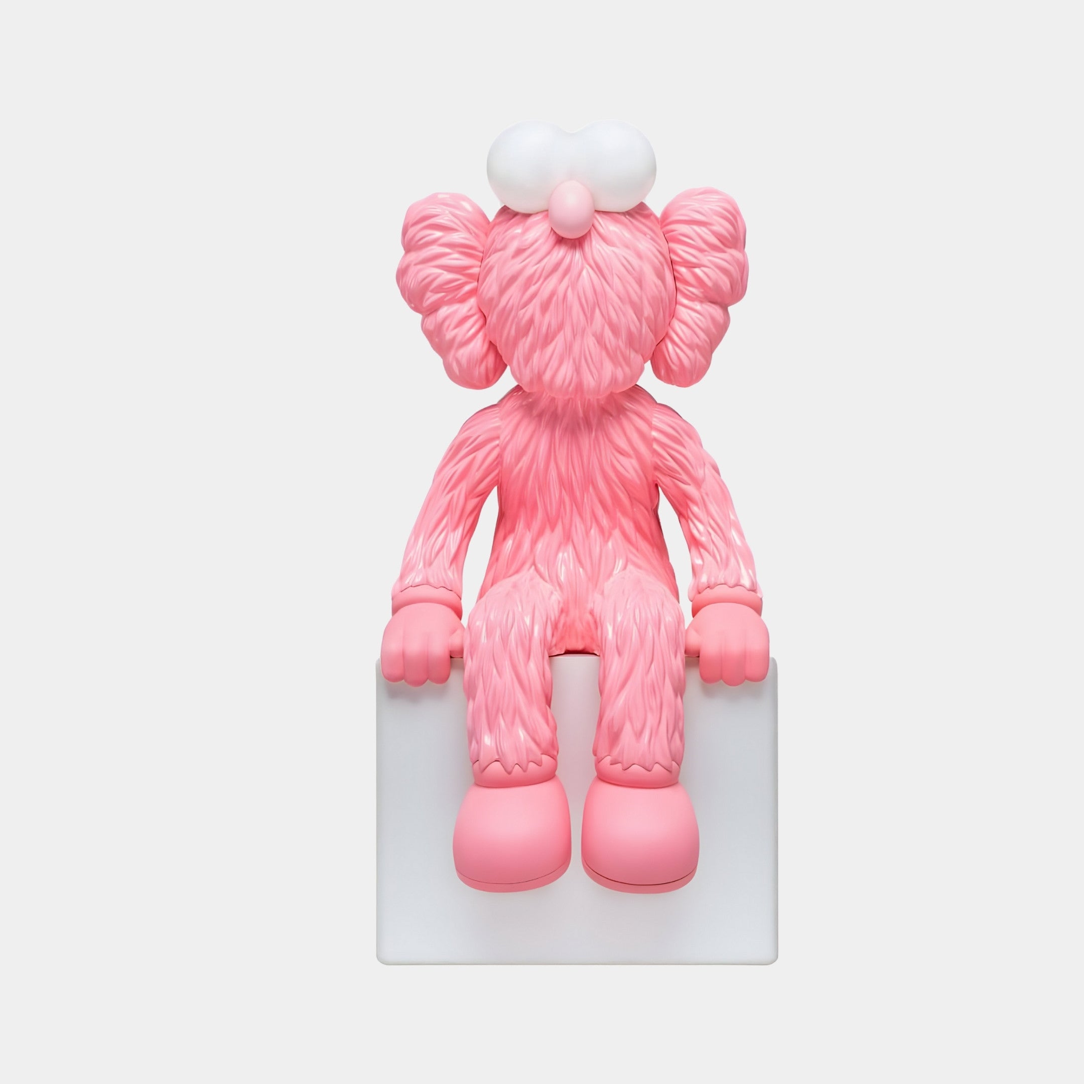 The Pedal Pink Iconify Furry Sitting Sculpture by Giant Sculptures features a pink, furry character with large ears and big shoes, accented in white, sitting on a white block. The cartoonish design embodies contemporary artistry against a plain white background.