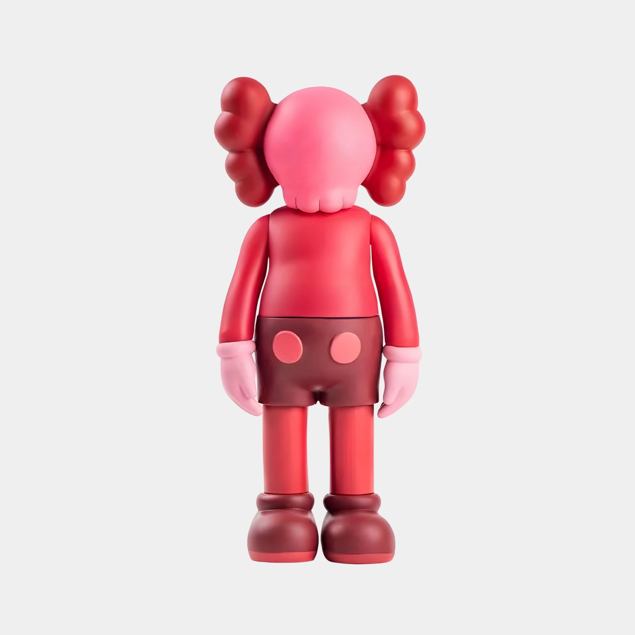 The Blush Ruby Iconify Standing Sculpture - 70cm by Giant Sculptures showcases a pink and red cartoon-like figure with large round hands, puffy ears, red shorts, and rounded shoes. Set against a plain white backdrop, its ideal for modern interiors.