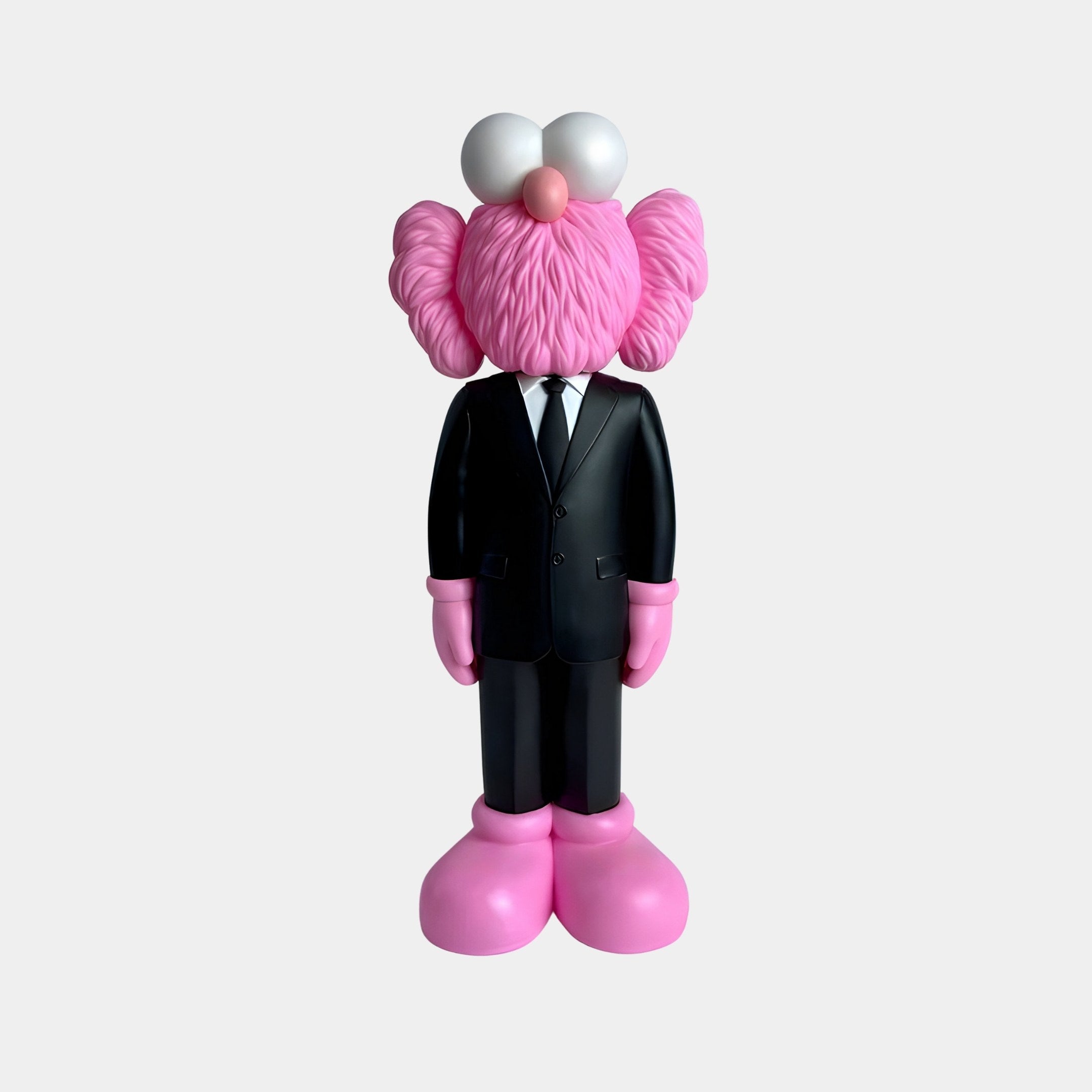 This modern Black Suit Iconify CEO Sculpture by Giant Sculptures, at 90cm, features a character in a sleek black suit with white shirt and tie, pink fur, large round white eyes, and pink shoes against a white backdrop.