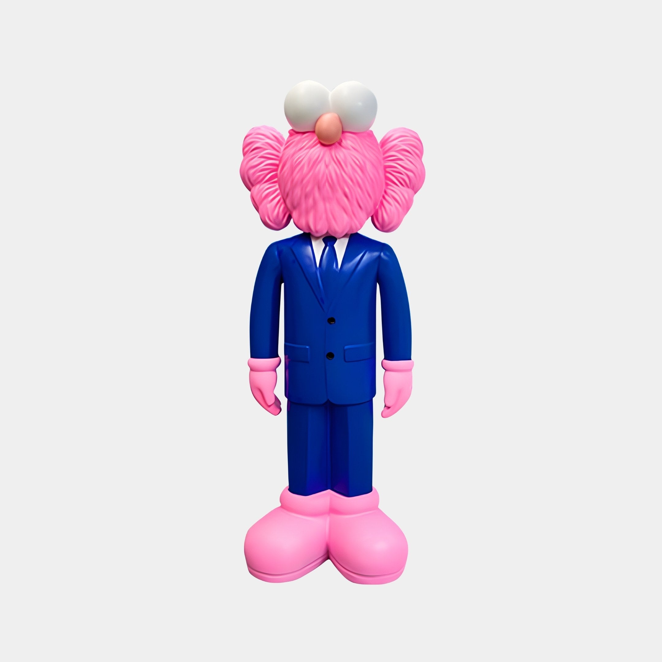 A pink creature with fuzzy hair and big white eyes stands upright, adorned in a Cobalt Blue Suit from the Iconify CEO Sculpture collection by Giant Sculptures, complete with pink gloves and oversized shoes, embodying contemporary artistry against a light gray background.