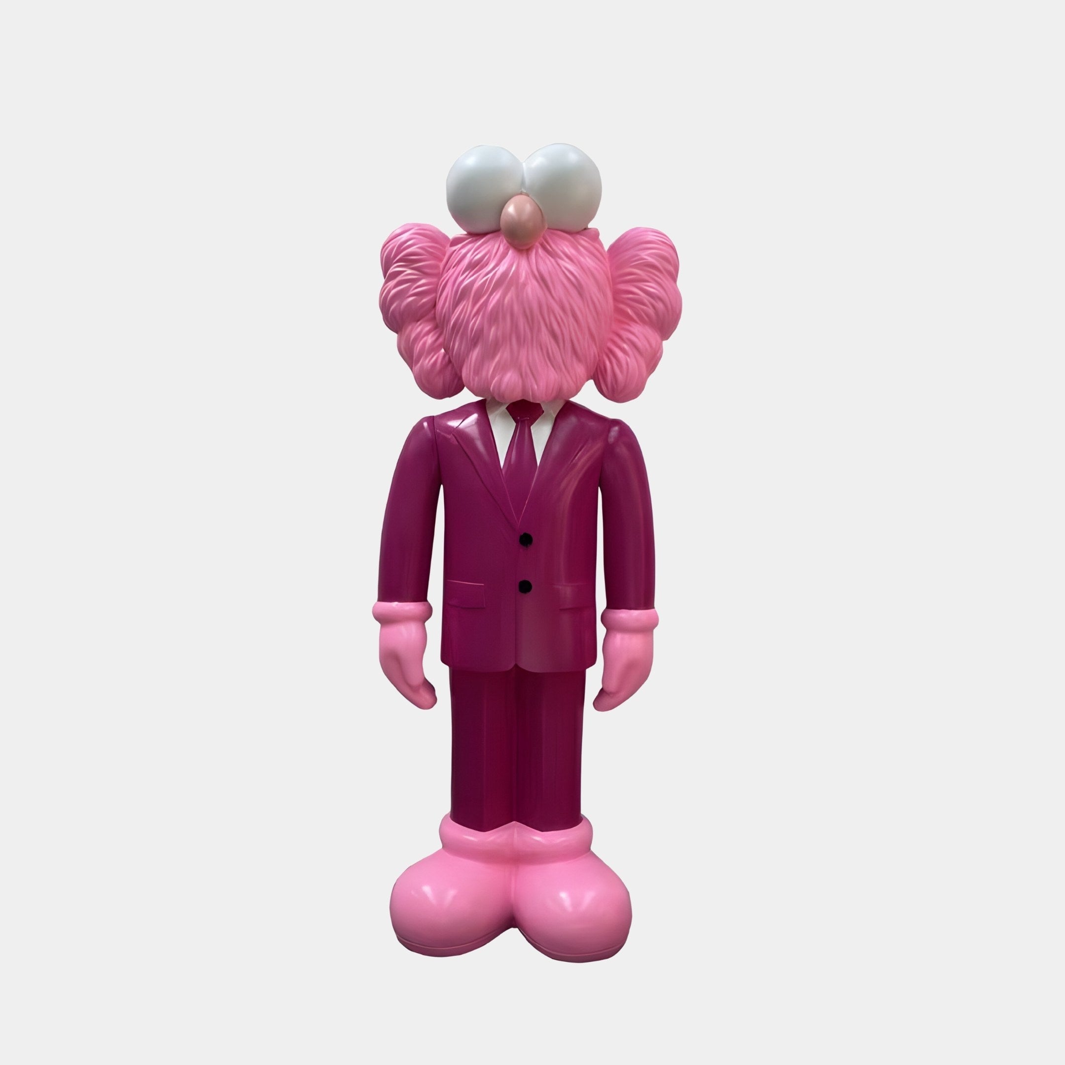 The Deep Magenta Suit Iconify CEO Sculpture (90cm) by Giant Sculptures is a whimsical pink cartoon-style figure resembling an Elmo-like character. It features a fluffy head, large eyes, and oversized pink shoes, standing against a plain gray background.