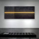 The Eternia Midnight Textured Oil Painting LED Wall Art by Giant Sculptures features a minimalist black textured surface with a central horizontal line of warm yellow light enhanced by LEDs, mounted on a white wall with a black tufted bench in front.