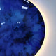 The Genesis Ocean 3D Resin Crystal Porcelain LED Wall Art by Giant Sculptures features a vivid blue circular design with marbled patterns, ocean-inspired themes, and a glowing yellow LED ring, creating an elegant effect against the white background.