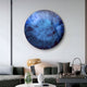 A modern living room features the Genesis Ocean 3D Resin Crystal Porcelain LED Wall Art by Giant Sculptures, showcasing ocean-inspired shades of blue and purple. The space also includes a gray sofa, a unique gold lamp, and decorative items like a glass bowl and tray on the coffee table.