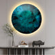 The Genesis Midnight 3D Resin Crystal Porcelain LED Wall Art by Giant Sculptures is mounted on a wall, featuring a round abstract design with blue and green hues and a glowing halo effect. Below it, a minimalist shelf displays a small vase with branches, two books, and a stylized rhino figurine.