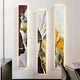 The Floren Golden Veil Canvas LED Wall Art by Giant Sculptures features three vertical panels with swirling patterns of maroon, white, black, gold, and orange textures. These abstract panels emit a warm backlit glow. Chairs and a tabletop are partially visible in the foreground.