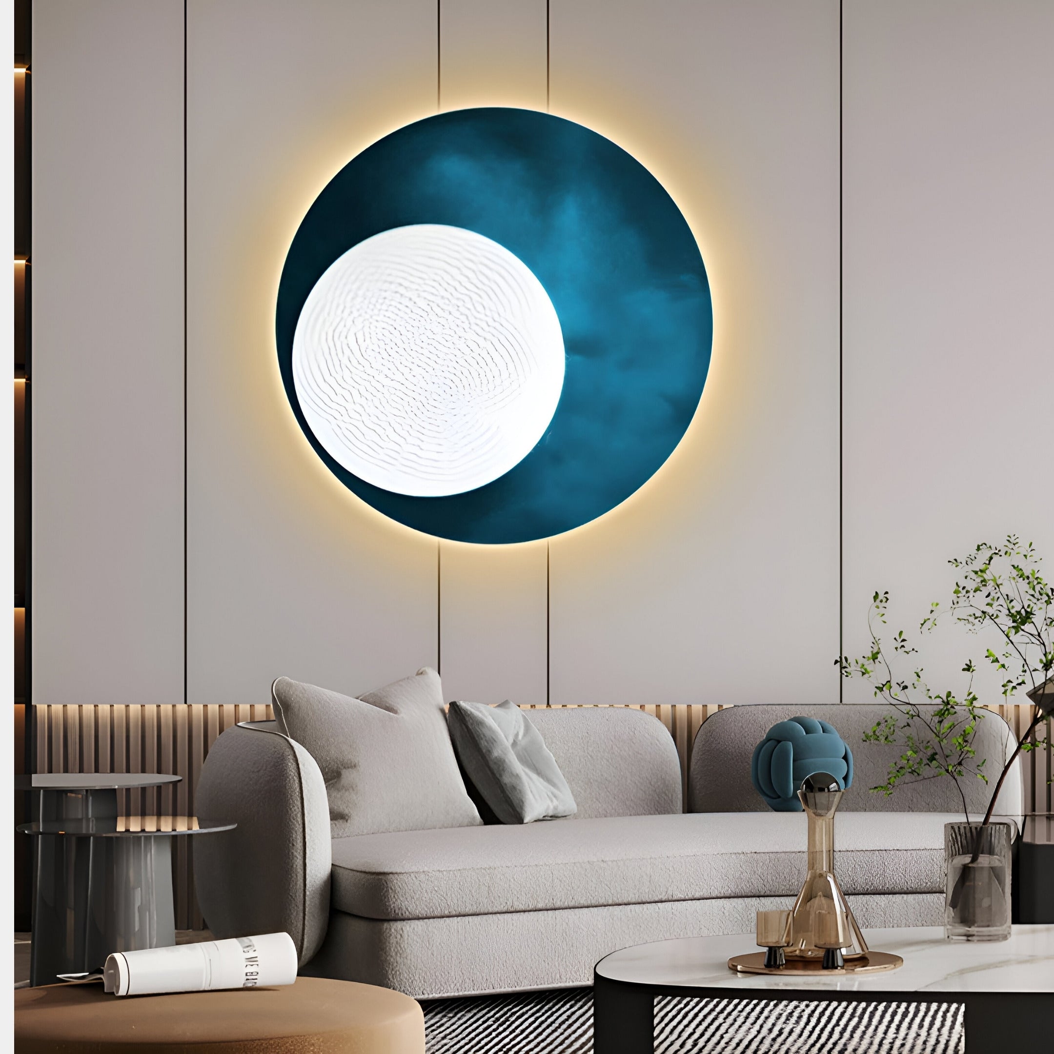 In a modern living room with a light grey curved sofa and minimalist décor, the Flaria Ocean 3D LED Wall Art Geometric Sandstone by Giant Sculptures is illuminated in blue and white, creating a focal point. A small table and potted plant balance the elegant setting.