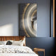 A modern bedroom features a gray and white palette with a neatly made bed and decorative pillows. The Celeste Orbit Glow LED Wall Art by Giant Sculptures, showcasing metallic and fiery swirls, hangs above the bed. Soft natural light enhances the serene ambiance of the modern interior.