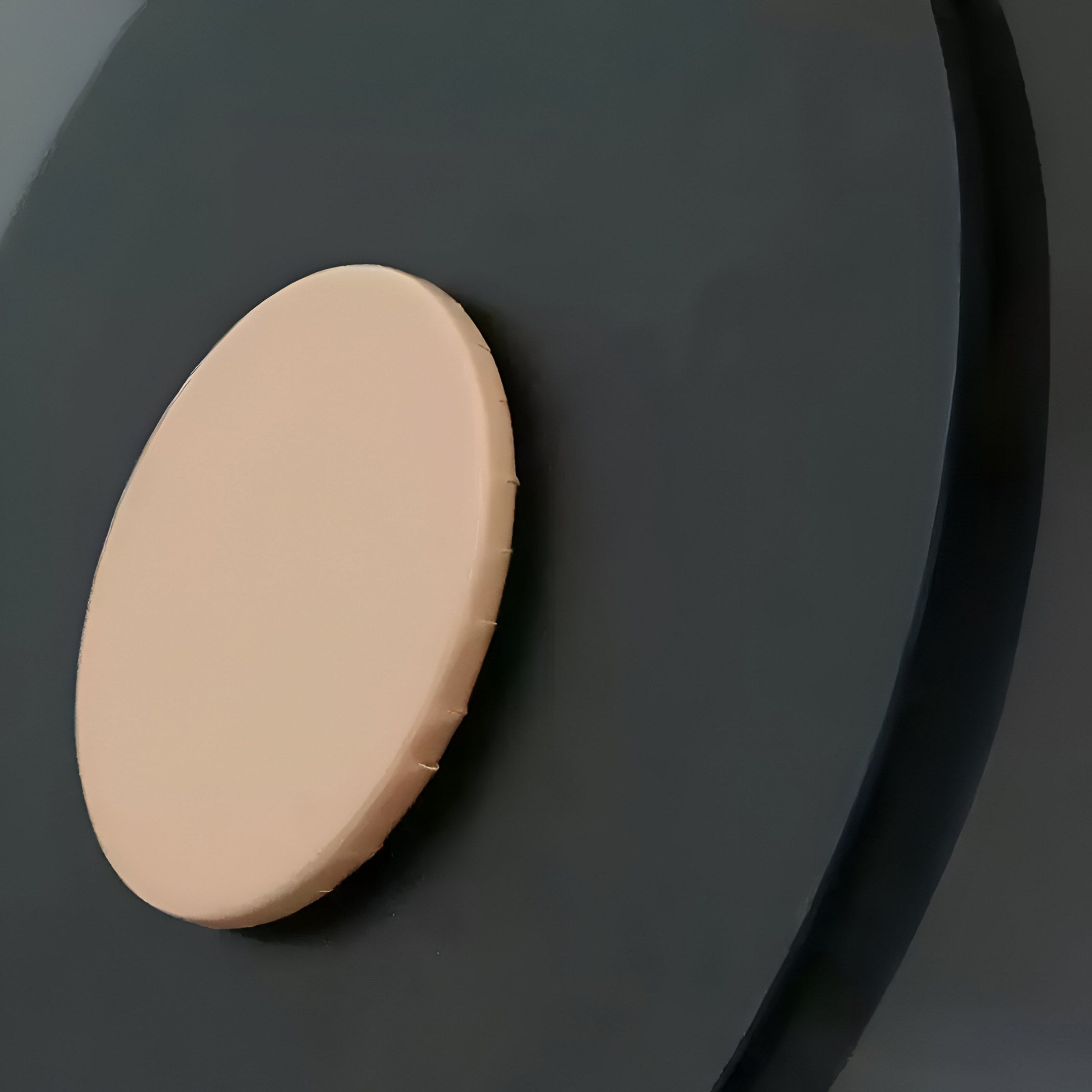 Close-up of a beige circular object on a dark green curved surface, showcasing the minimalist elegance of Giant Sculptures Eclipse I Charcoal Bronze Acrylic 3D LED Wall Art with its striking geometric composition and contemporary design.