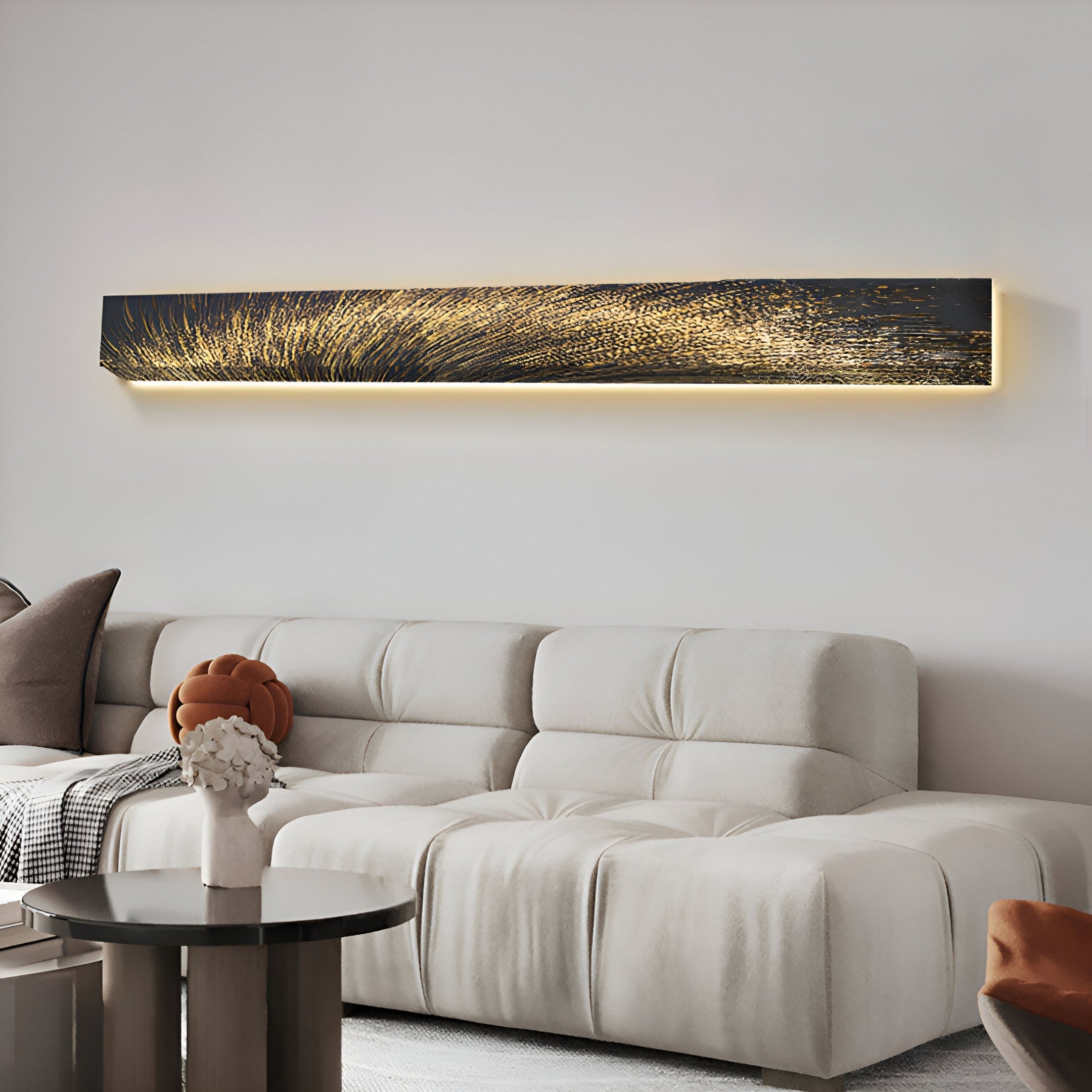 A modern living room includes a white tufted sofa with cushions, a round black side table adorned with decor, and the Giant Sculptures Radiance Golden Canvas LED Wall Art above, casting warm gold ambient light.