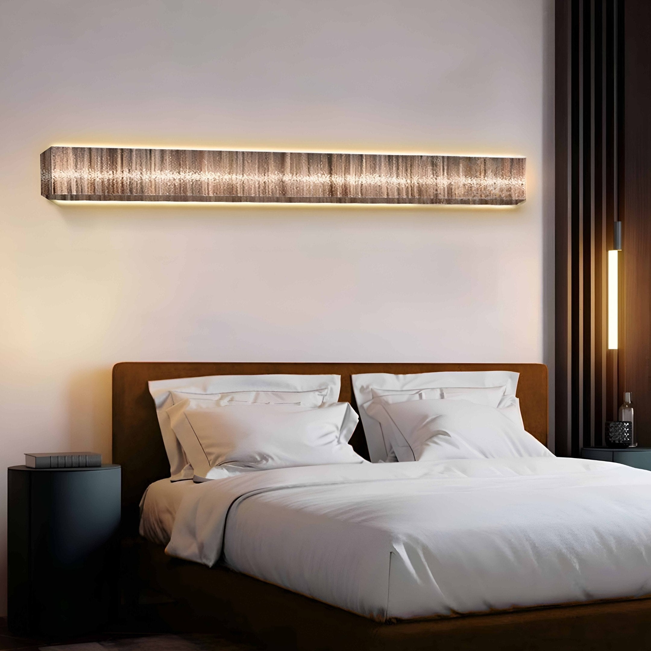 A modern bedroom showcases the Radiance Sandy Gold Canvas LED Wall Art by Giant Sculptures above the bed, emitting a gentle glow. The white-bedded brown-framed bed is flanked by black nightstands with small lamps, creating coastal warmth with its minimalist decor and warm lighting.