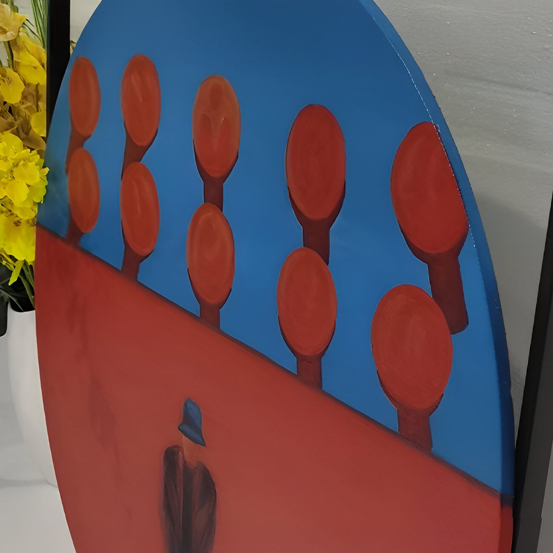 The Orion Crimson Silhouettes Oil Painting LED Wall Art by Giant Sculptures features a person in a blue hat and dark coat facing stylized trees with round canopies, against a vivid blue sky, crimson ground silhouettes, and yellow flowers on the left.