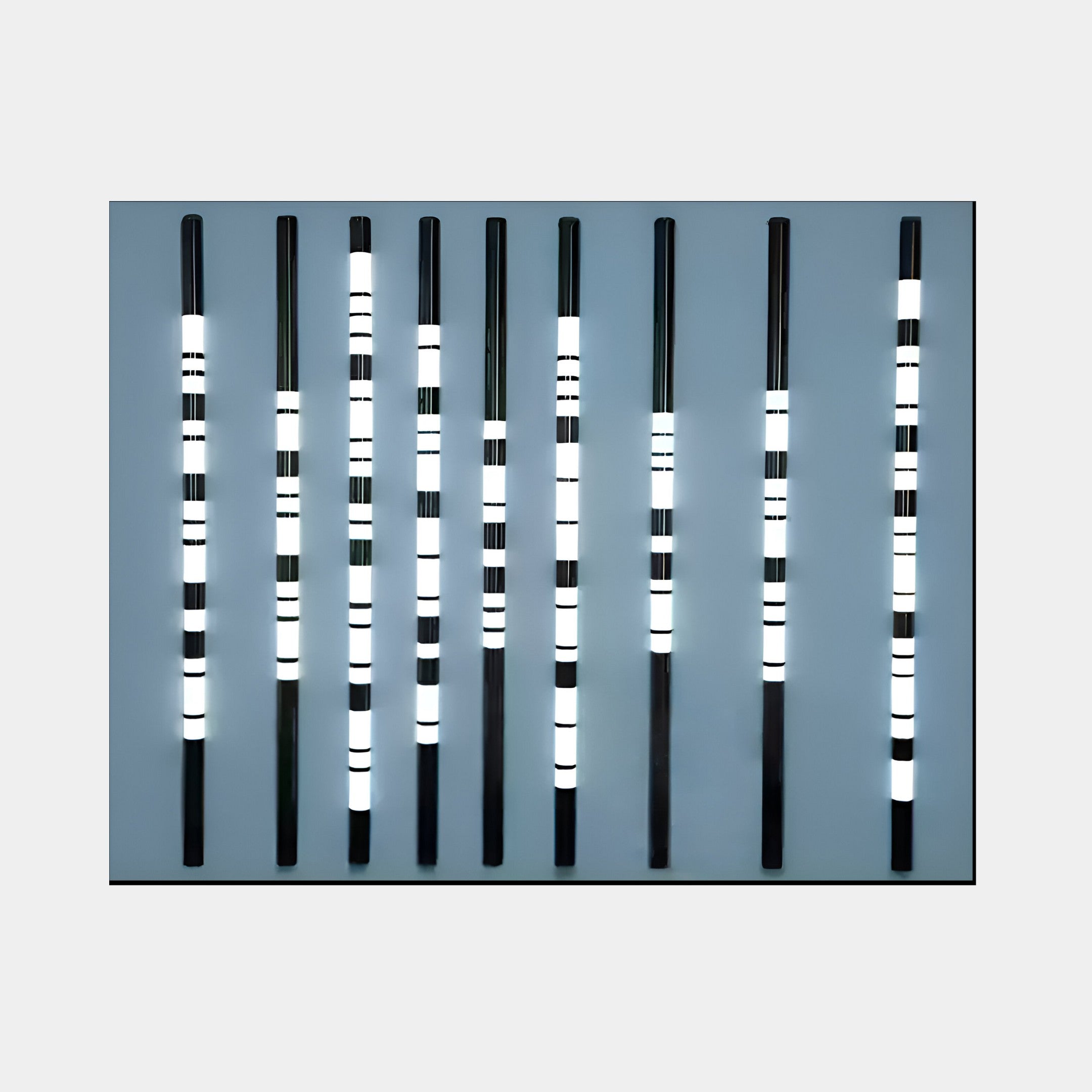 The Strata Steel Blue LED Wall Art by Giant Sculptures features installation art with nine vertical black bars on a steel blue background, illuminated to create glowing horizontal stripes, exemplifying modern design.