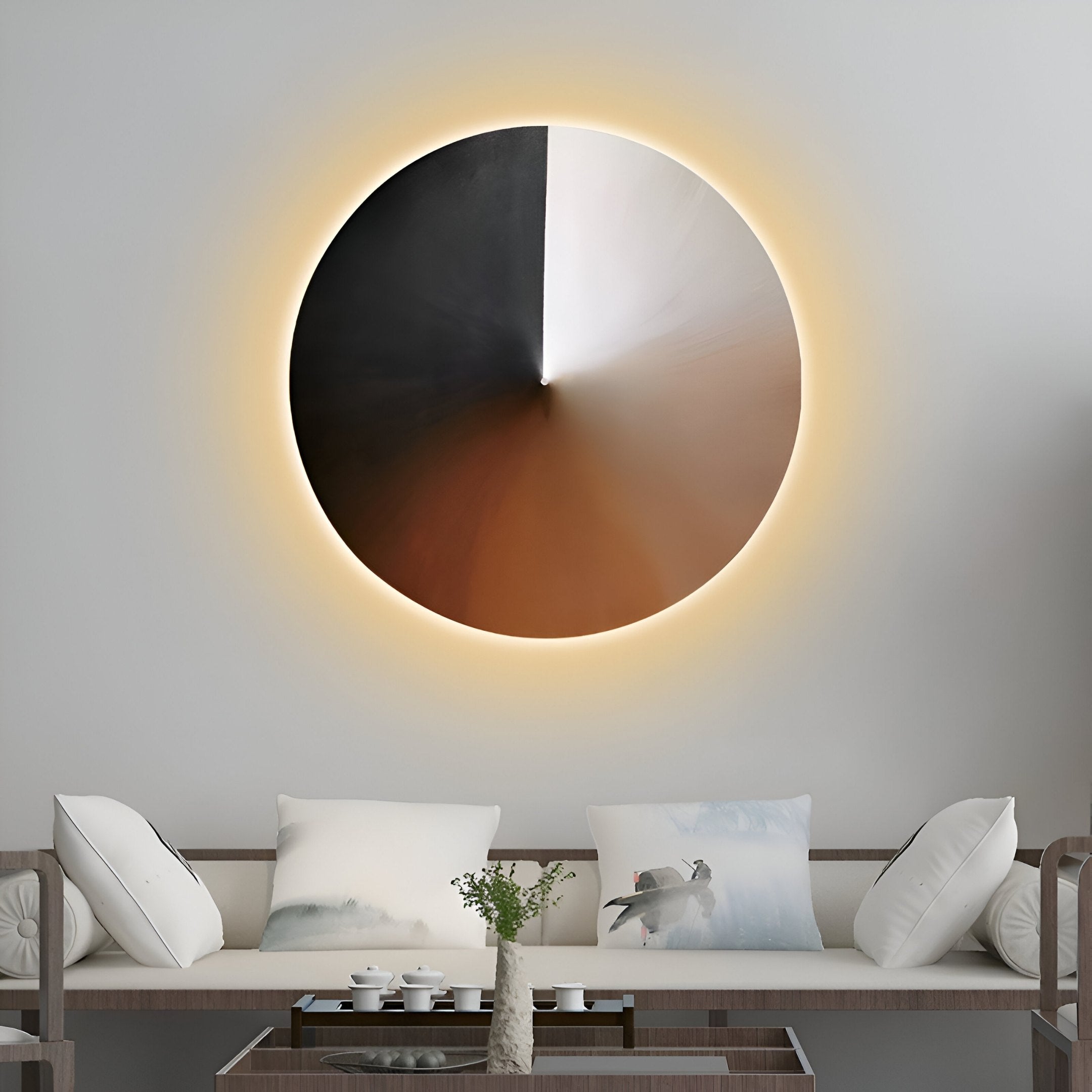 A modern living room showcases the Orbit Copper Hand-Painted Canvas 3D LED Wall Art by Giant Sculptures, featuring gradient black to brown colors with a warm light halo. Below, a minimalist couch with white and scenic-themed pillows is paired with a small coffee table displaying decorative items.