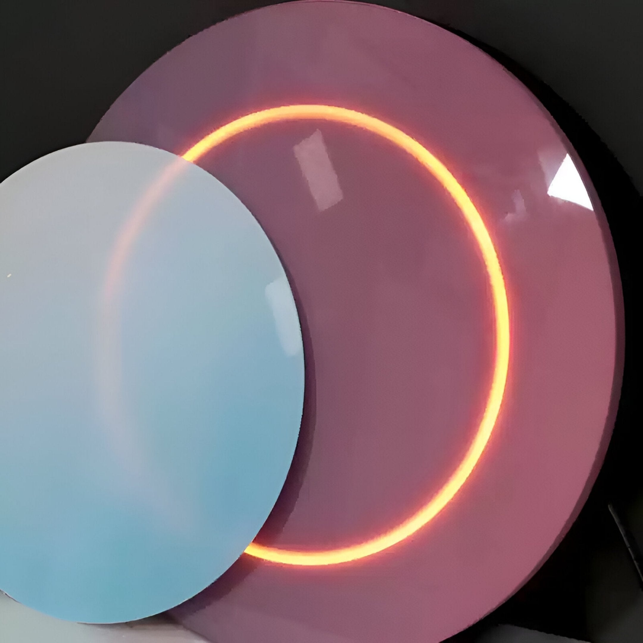 A reflective blue disc, reminiscent of the Lunar Blush Sky Crystal Porcelain 3D Yellow LED Wall Art by Giant Sculptures, partially overlaps a larger glowing pink disc with an illuminated orange ring at its center against a dark background.