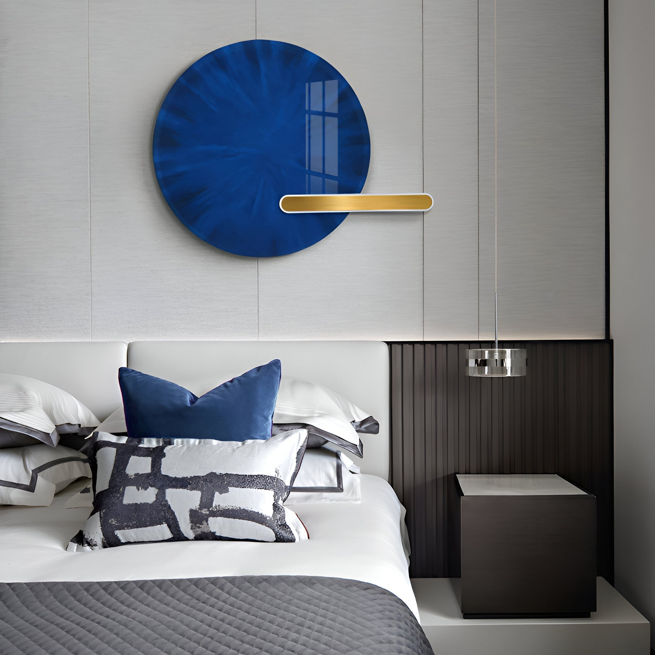 A modern bedroom features a bed with white and gray linens, blue and patterned pillows, and a minimalist nightstand under an LED crystal porcelain pendant light. The Lumea Sapphire 3D Wall Art by Giant Sculptures adds a splash of color, enhancing the rooms sophisticated aesthetic.