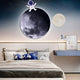 A bedroom showcases a cosmic decor, featuring a moon mural above the bed and Giant Sculptures Cosmos Astronaut Dream UV Wood Carving LED Wall Art. Space motif pillows adorn the bed, while LED lighting enhances the ambiance. A desk with a lamp and framed picture completes the look.