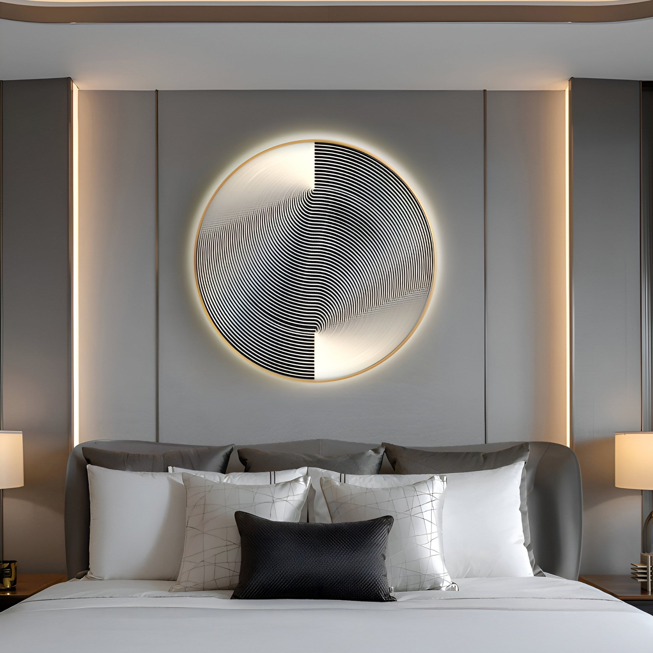 A modern bedroom with a sleek bed and white/gray pillows creates serenity. The Astral Silver Crystal Porcelain LED Wall Art by Giant Sculptures above displays concentric black/white lines on the minimalist gray wall, flanked by two table lamps enhancing its modern vibe.