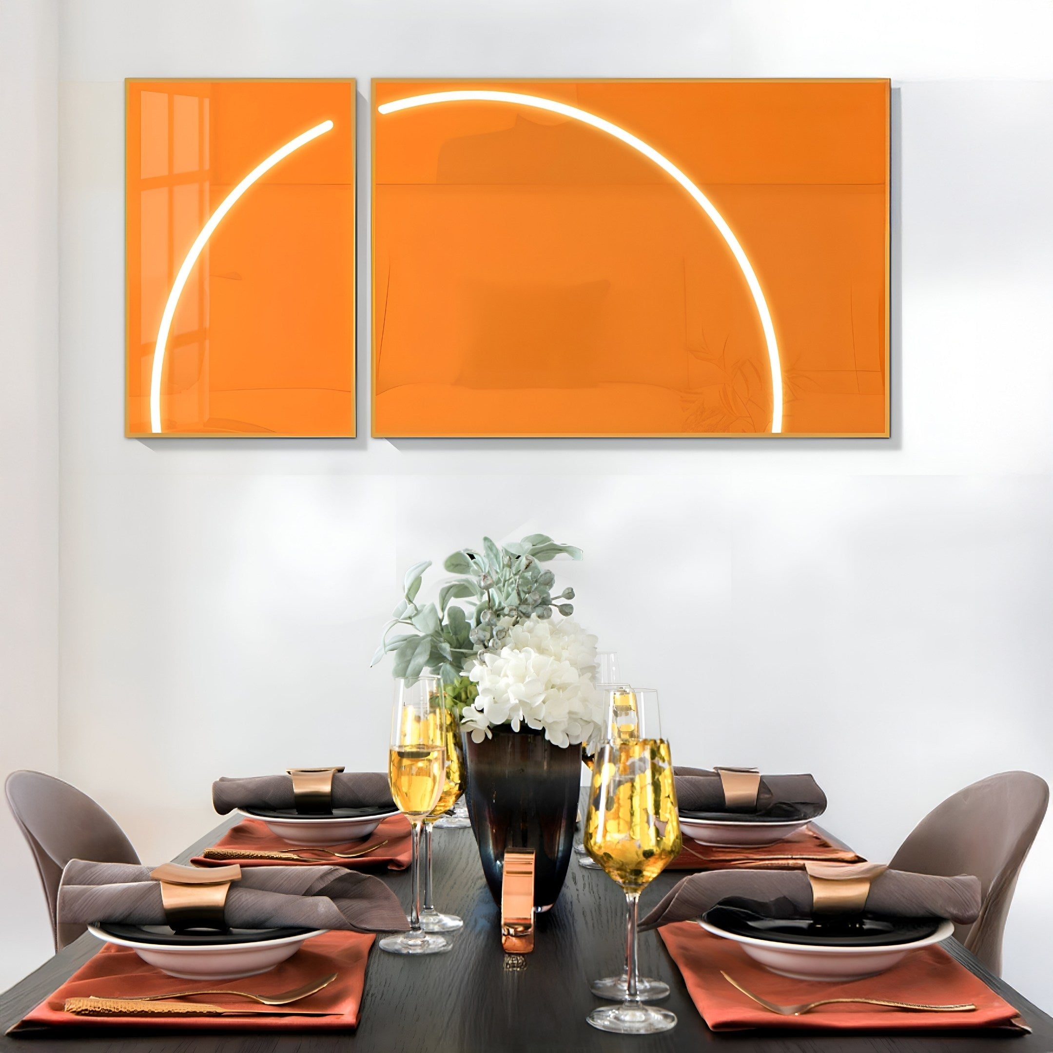 A modern dining room features a dark table with brown napkins, gold cutlery, and champagne flutes. Giant Sculptures Enigma Amber Sunrise LED wall art adds vibrant color above, while a floral vase elegantly centers the design.