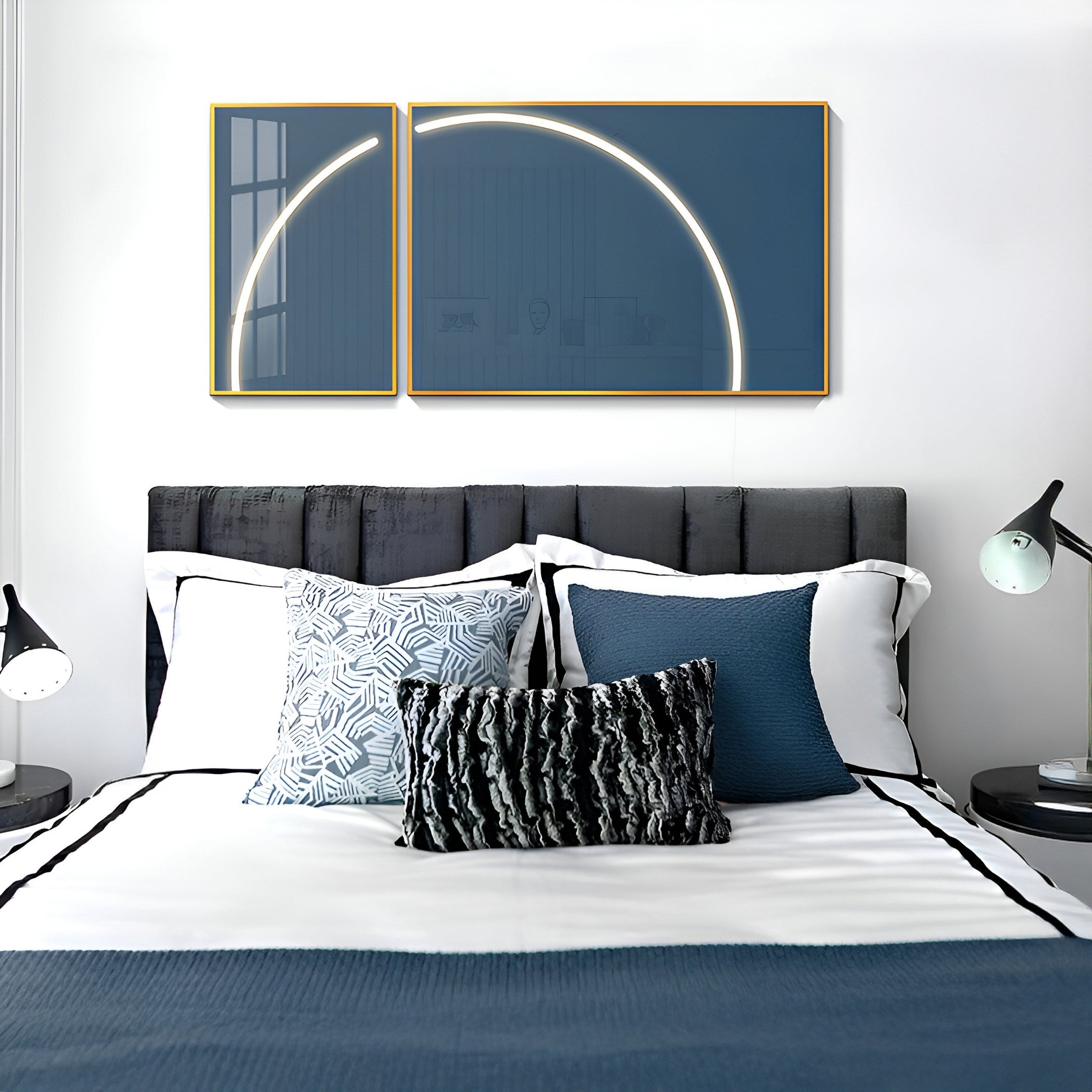 A neatly made bed with white and blue bedding, various pillows, and two abstract framed artworks is illuminated by Giant Sculptures Enigma Midnight Teal LED Wall Art, displaying a glowing circle. Midnight Teal accents enhance the room alongside two black lamps flanking the bed.