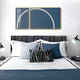 A neatly made bed with white and blue bedding, various pillows, and two abstract framed artworks is illuminated by Giant Sculptures Enigma Midnight Teal LED Wall Art, displaying a glowing circle. Midnight Teal accents enhance the room alongside two black lamps flanking the bed.