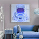 A cozy room features a blue sofa and toy-laden side table. Above, the Giant Sculptures Stellar Electric Sapphire Acrylic 3D LED Wall Art displays an astronaut motif with neon starry lights, contrasting beautifully with the cloud-shaped ceiling lamp.