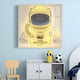 The Stellar Auric Gold Acrylic 3D LED Wall Art by Giant Sculptures, featuring a bright yellow astronaut helmet with a starry sky visor, is displayed on a light blue wall above a white cabinet with books and a penguin bottle, alongside a small chair and bed with a black-and-white soccer ball.