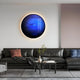 A modern living room features a dark gray leather sofa with a pink and black pillow. Above it, Giant Sculptures Galaxia Neptune Crystal Porcelain LED Wall Art adds an ethereal glow. A coffee table with a vase and plant completes the stylish setting.