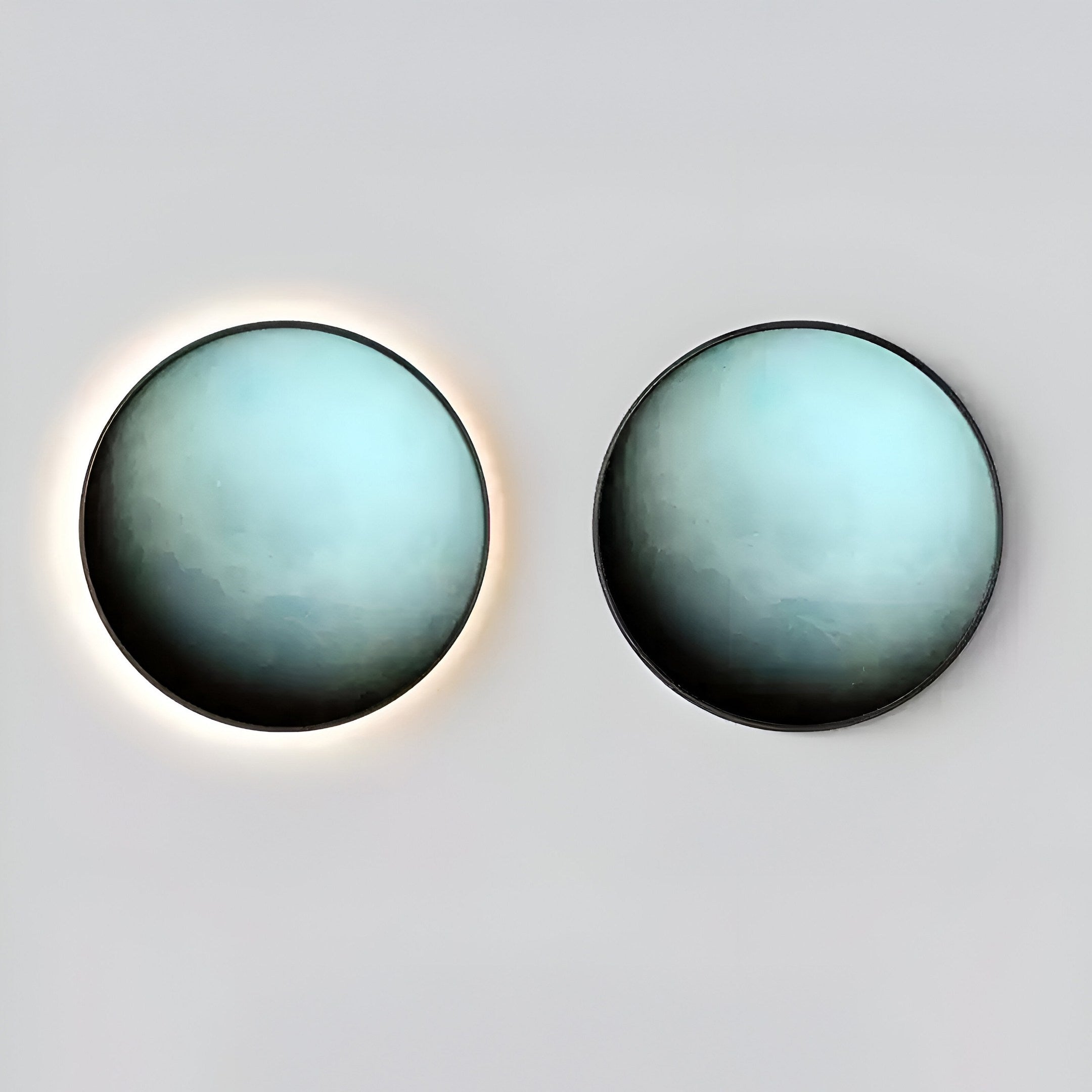 The Galaxia Uranus Crystal Porcelain LED Wall Art by Giant Sculptures features two circular lights: the left showcasing a celestial halo effect in blue and green, while the right offers minimalistic elegance against a neutral backdrop.