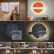 A composite image shows a hand touching a light switch beneath three Aeon Sunset Ember Leather 3D LED Wall Art pieces by Giant Sculptures, each exhibiting geometric patterns and Sunset Ember hues. These artworks illuminate the sofas below with two darker pieces at the bottom and one bright piece on top.