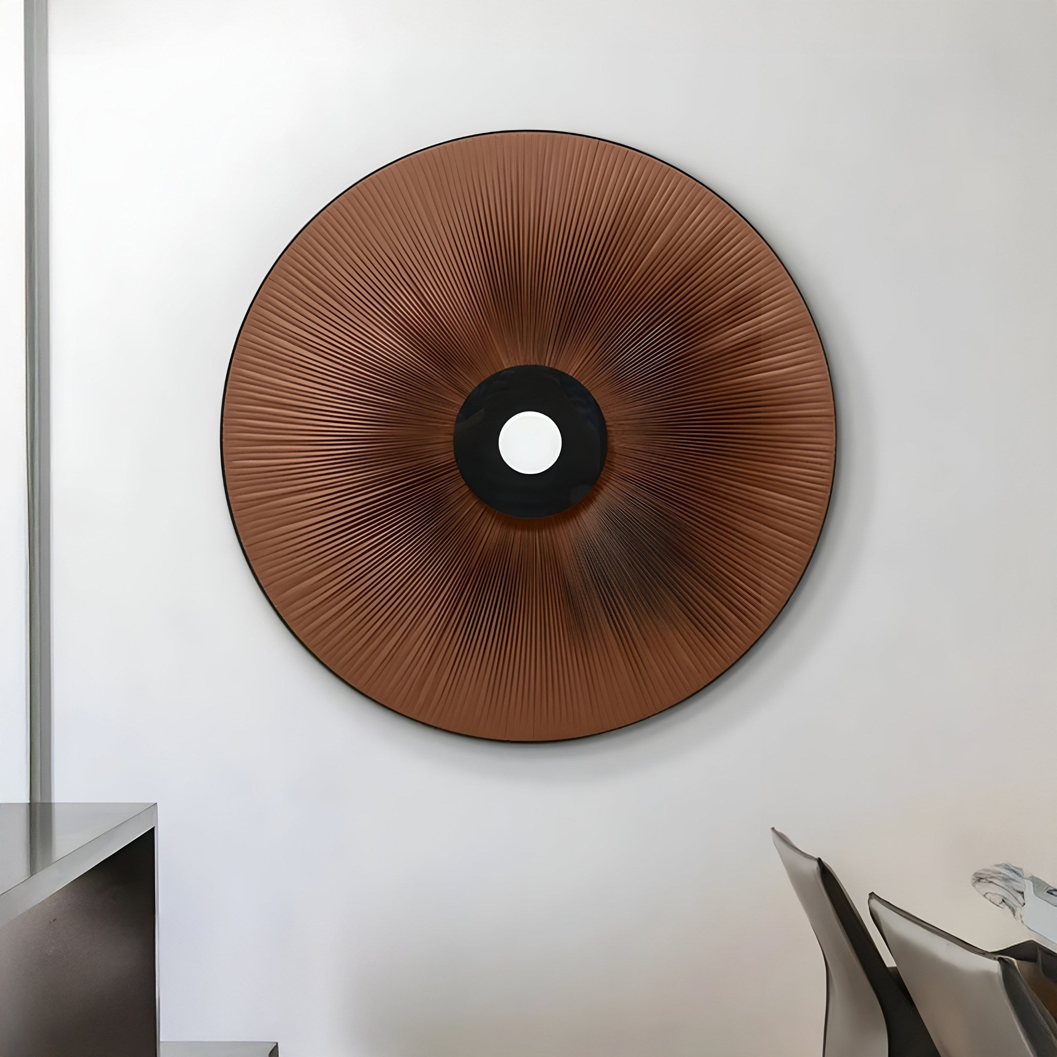 The Vanguard Mocha Bronze Leather 3D LED Wall Art by Giant Sculptures, featuring a large round textured design with a black center and small white circle, is mounted on a white wall. This timeless piece enhances the modern dining area, where a table and chairs are visible in the foreground.