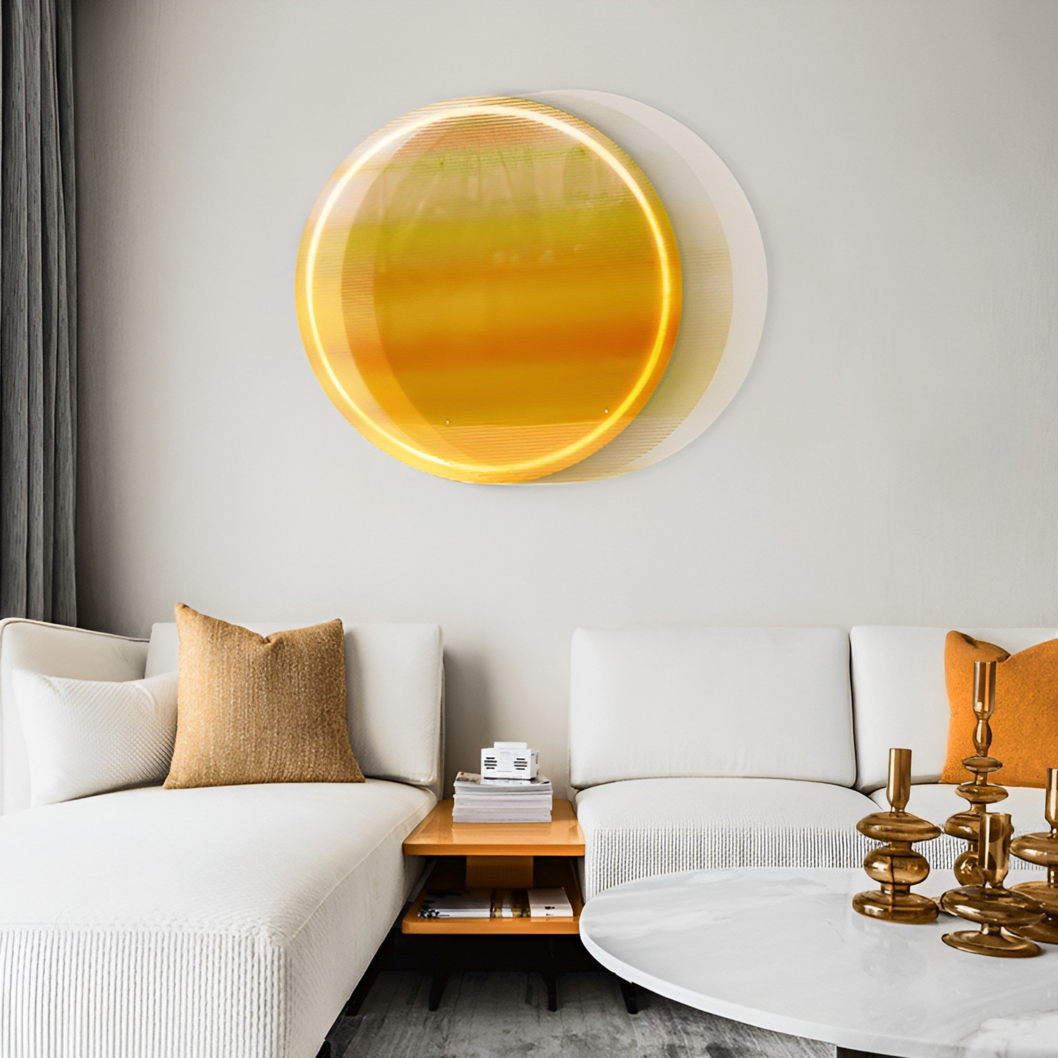 A contemporary living room features a white sectional sofa with a gold pillow, complemented by a round white coffee table and gold candle holders. The Chromia Golden Horizon Acrylic LED Wall Art by Giant Sculptures enhances the decor, while a wooden side table with books completes the look.